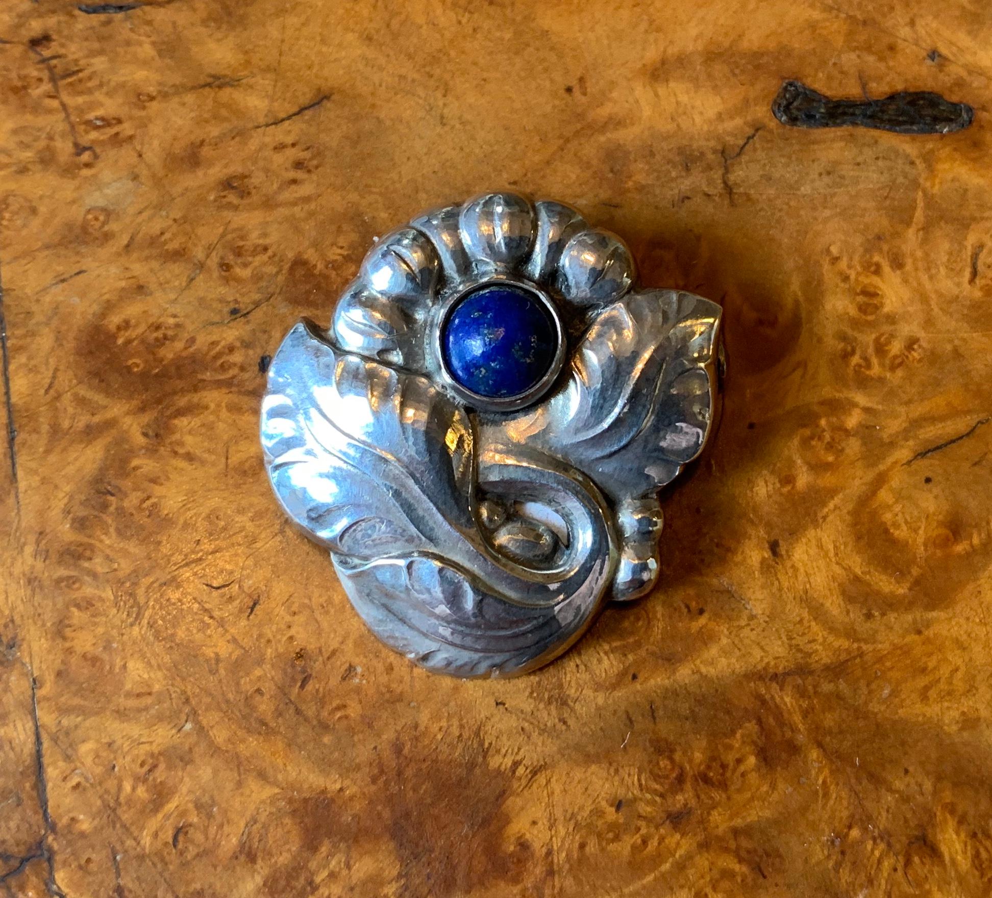 This is the gorgeous early (1933-1944) Georg Jensen sterling silver pin brooch in the form of a flower set with a stunning blue Lapis Lazuli gem. The brooch has the early Jensen mark of JG in a rectangle and is number 71.
This pin is a wonderful