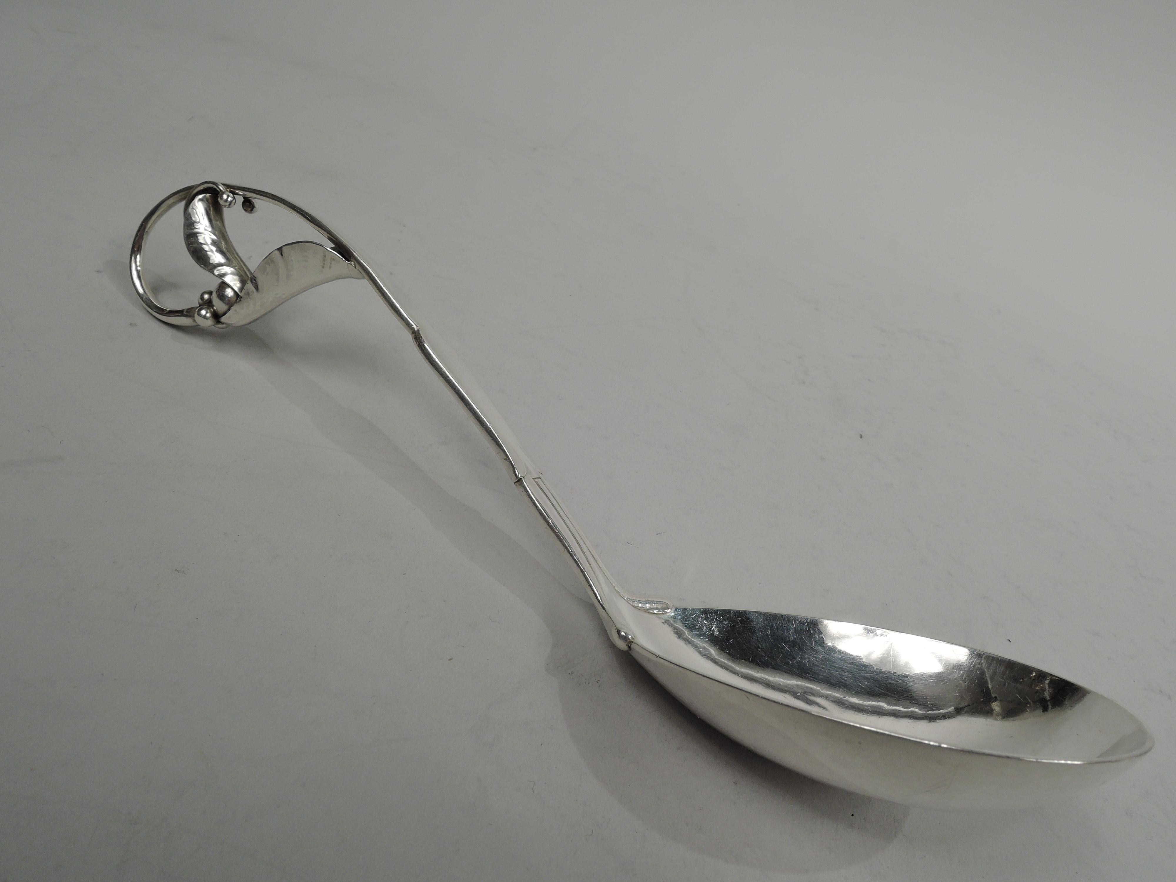 Ornamental 141 sterling silver serving spoon. Made by Georg Jensen in Copenhagen and imported to England in 1930 by George Stockwell. Oval bowl and shaped and tapering handle with turned-under leaf and tendril terminal. Fully marked including