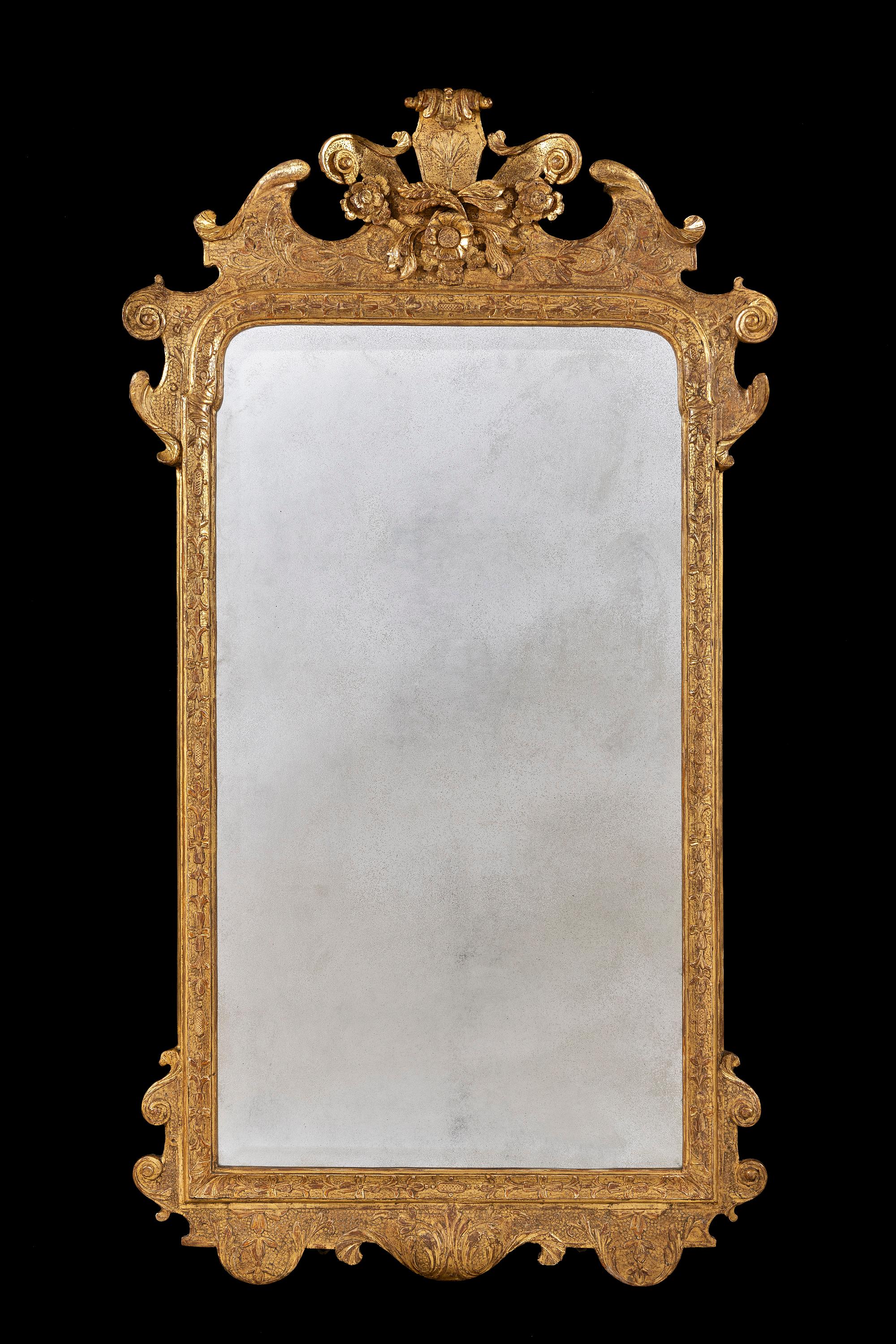 The mirror has an unusual central cartouche with carved volute, flower heads and foliage flanked by a swan neck pediment. The original bevelled mirror plate is framed by a concave moulding carved with bell flowers and flower heads above a similarly