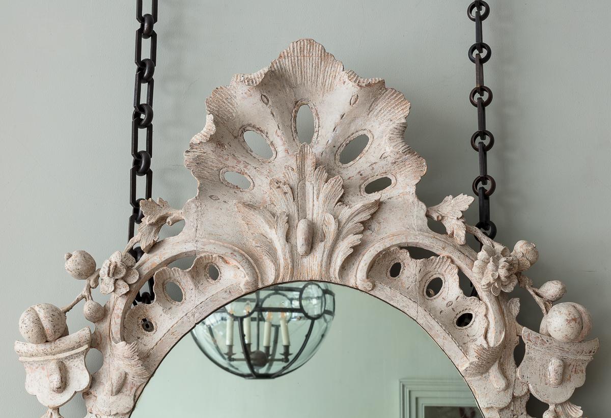 Uno specchio intagliato e dipinto di bianco del primo periodo di Giorgio II

Il piatto ovale con cornice traforata intagliata con acanto, volute a 'c' e dettagli foliati eseguiti con sicurezza, con smerlo traforato e cresta intagliata ad acanto.