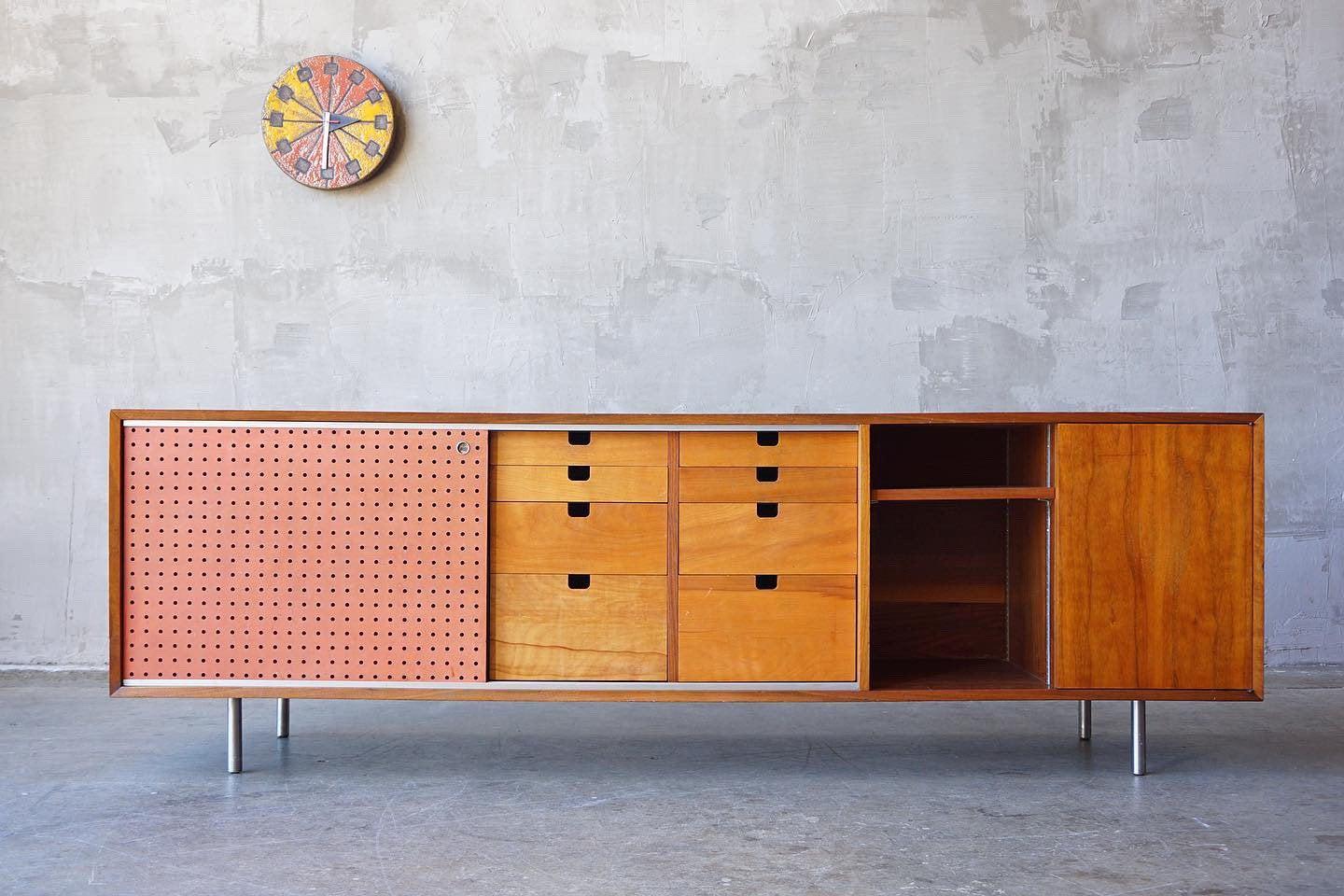 George Nelson cabinet in walnut with birch interior drawers and original coral red enameled pegboard sliding door. 

The adjustable interior shelves make it an ideal solution for media use. 

This piece is in very nice original condition with