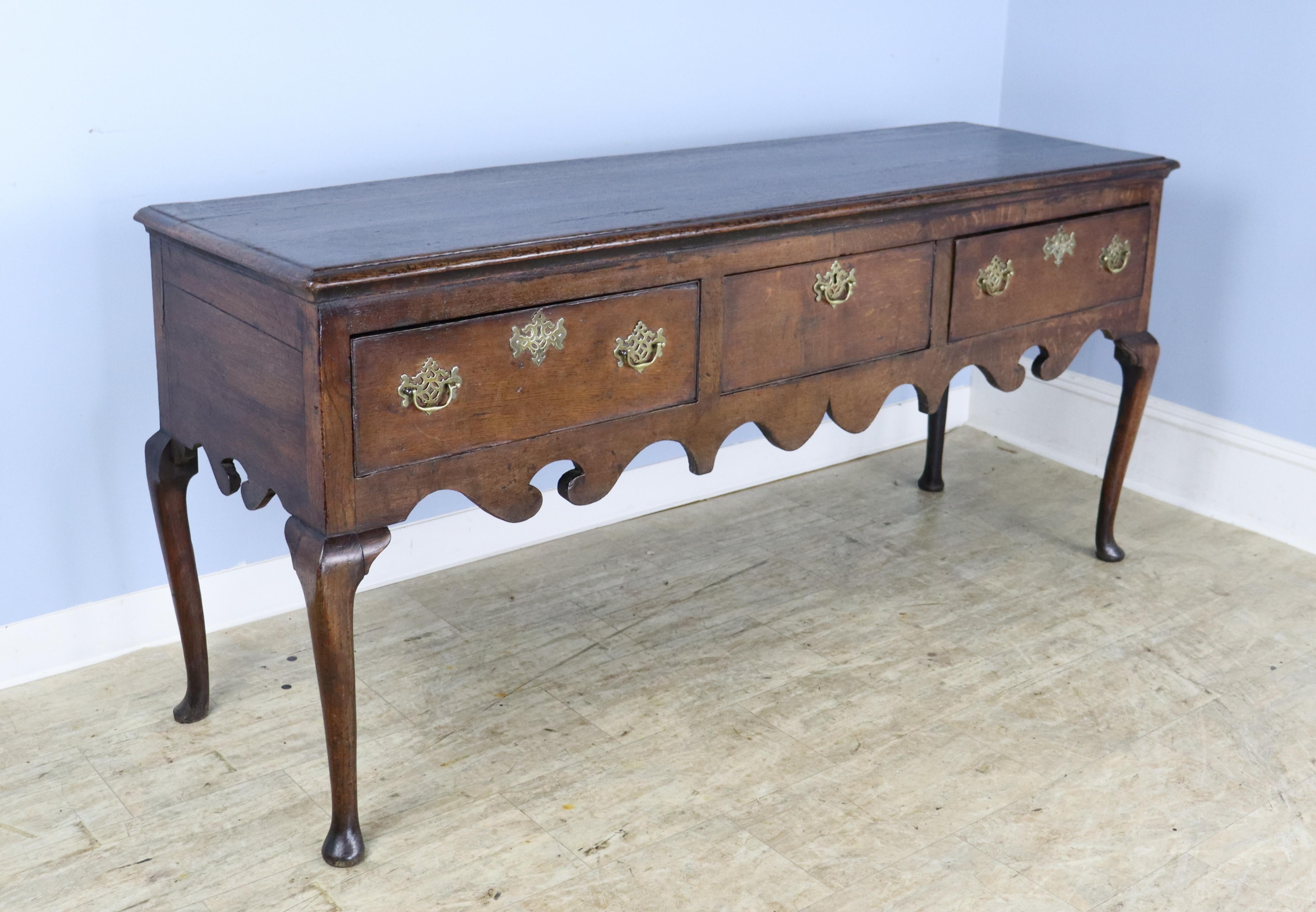 A long formal console table from the early 1700's.  This piece boasts lots of period detail, including gracious pad feet, a whimsical scalloped apron, curved cabriole legs and original fretted brass escutcheons.  The oak has good color and patina. 
