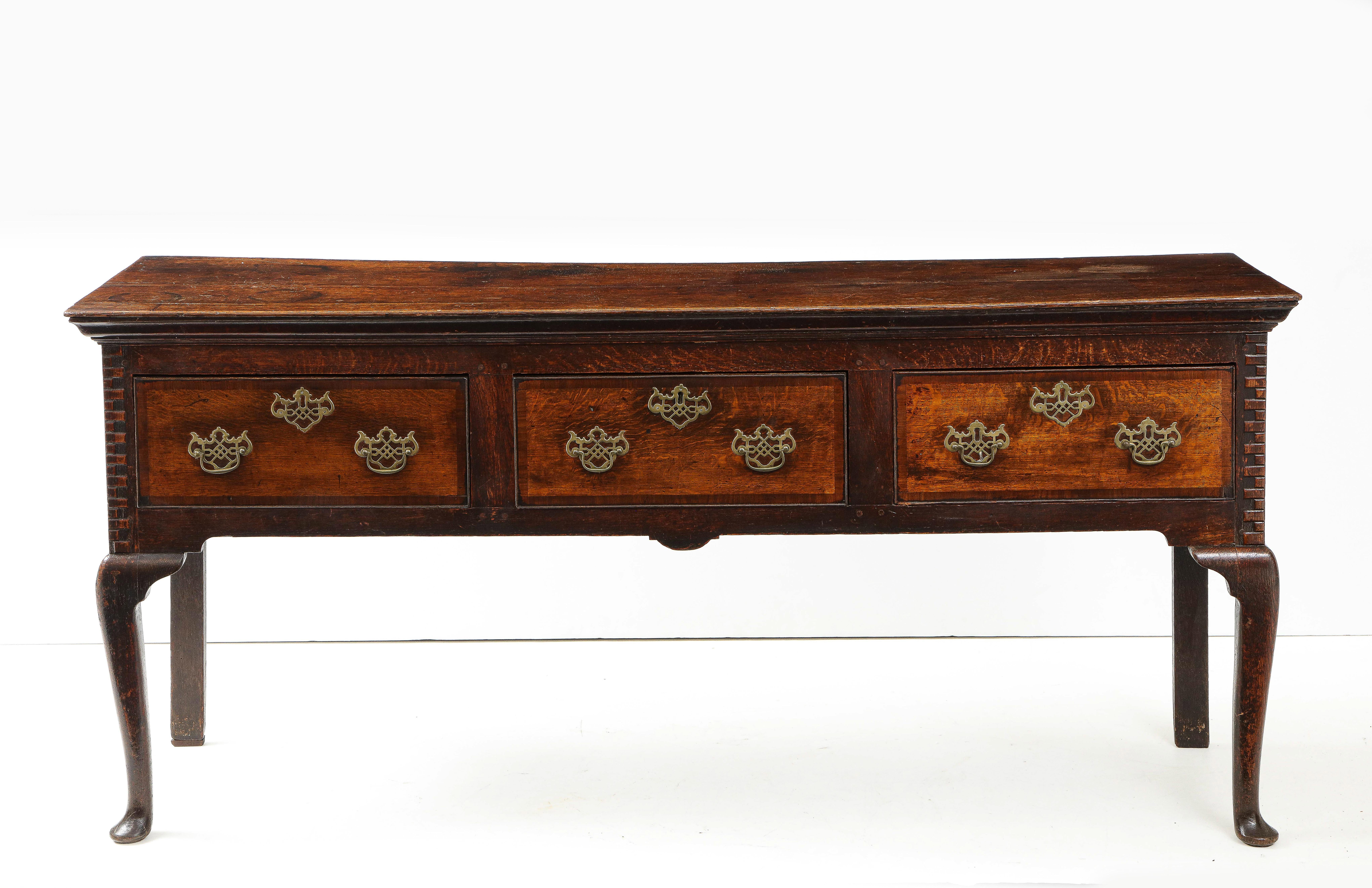 Fine George II period oak low dresser, the under-molded top over three drawers having mahogany banding and pierced brass hardware, the corners with brickwork quoin rustication, standing on cabriole legs ending in pad feet, the whole with good rich