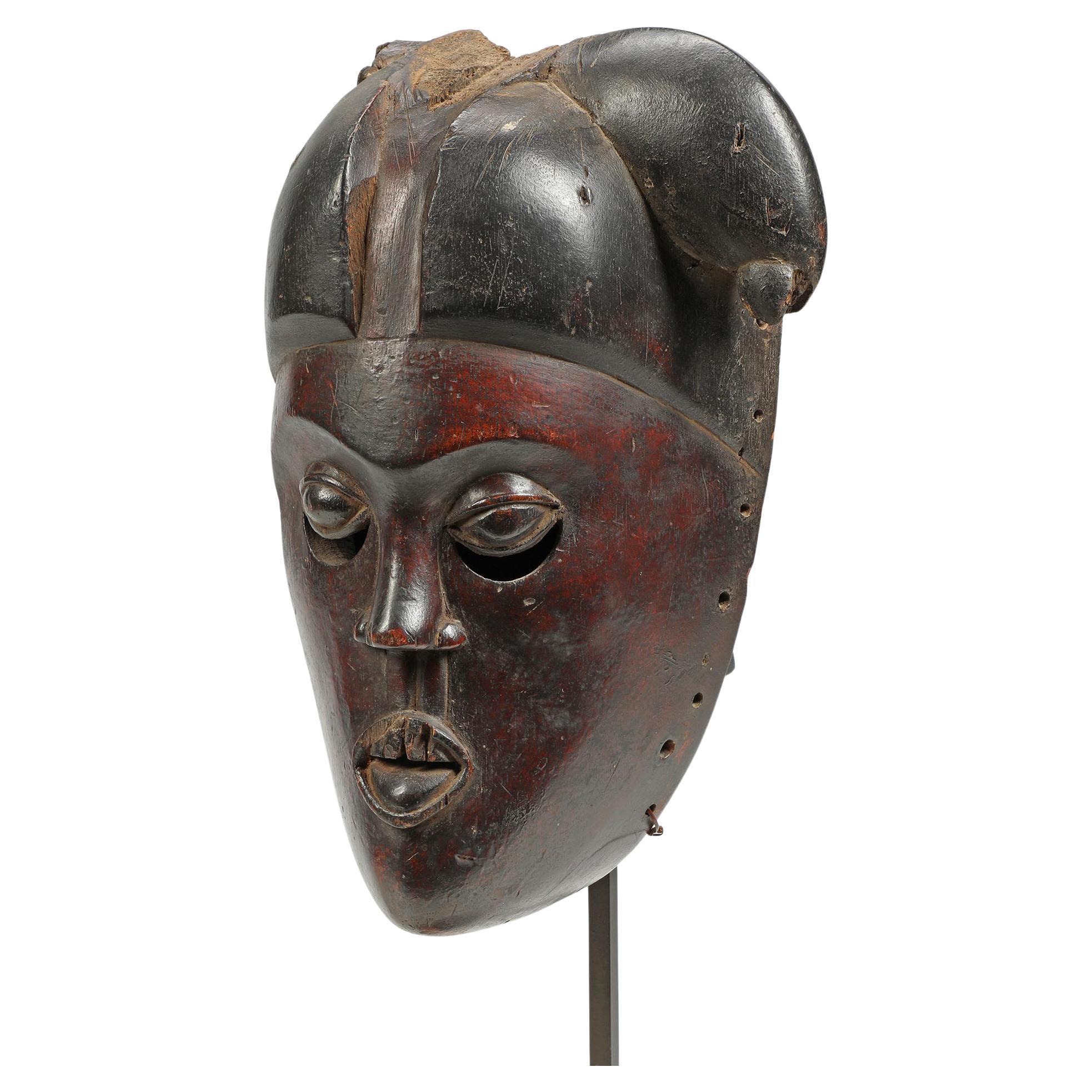 Fragment de masque Ibibio précoce du Nigeria, pigment noir-rouge profond, yeux expressifs. Un visage convaincant sur un support métallique personnalisé. Dégâts d'insectes anciens/érosion sur les cheveux droits et le côté du visage. Masque de 10,75