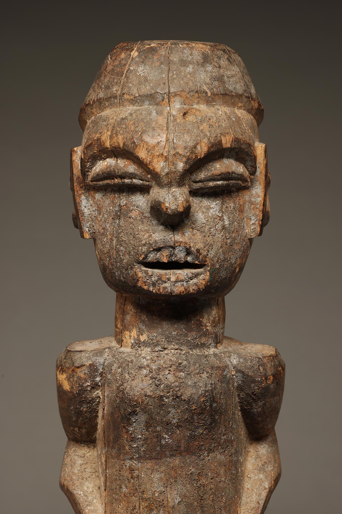 Early Ibibio standing carved wood male figure, powerful expression with hands on sides of stomach, exposed teeth and vertical raised scarification marks on sides of face.  From a shrine with the remains of encrusted offerings, weathering and