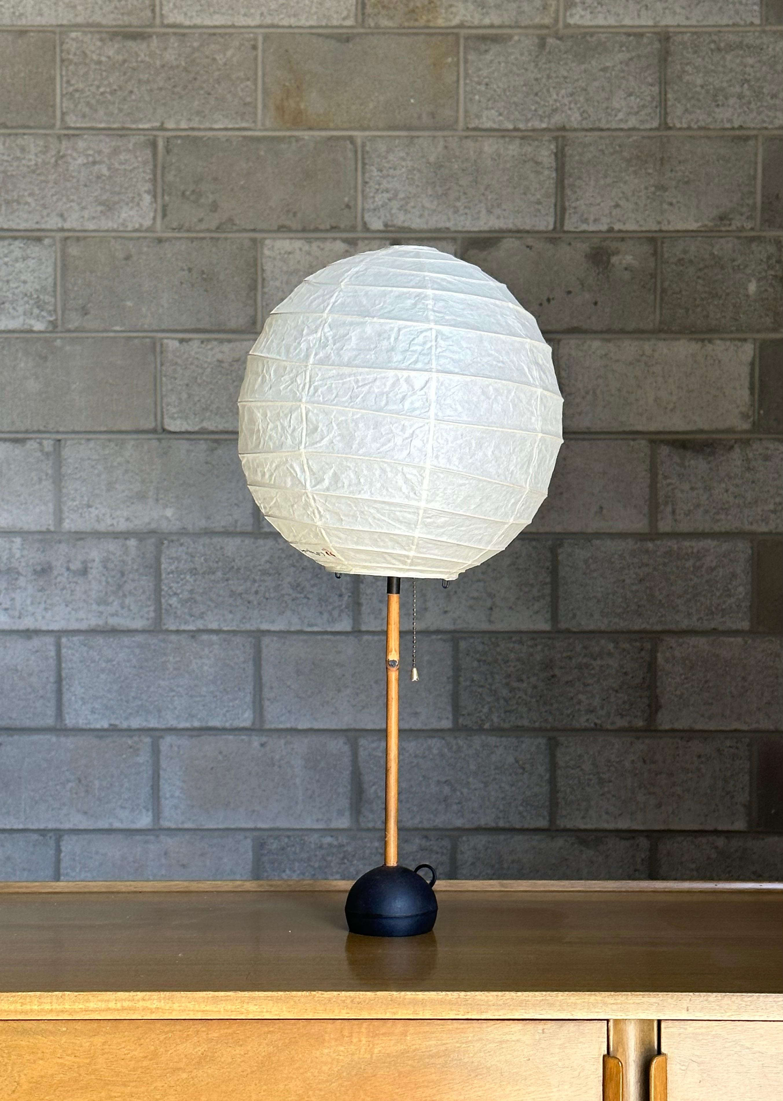 An early Isamu Noguchi Akari Light Sculpture circa 1960s. Light features an enameled cast iron base with bamboo rod, and shade consisting of washi paper. A truly beautiful organic modernist lamp. Shade and harp are both newer. Signed on base 