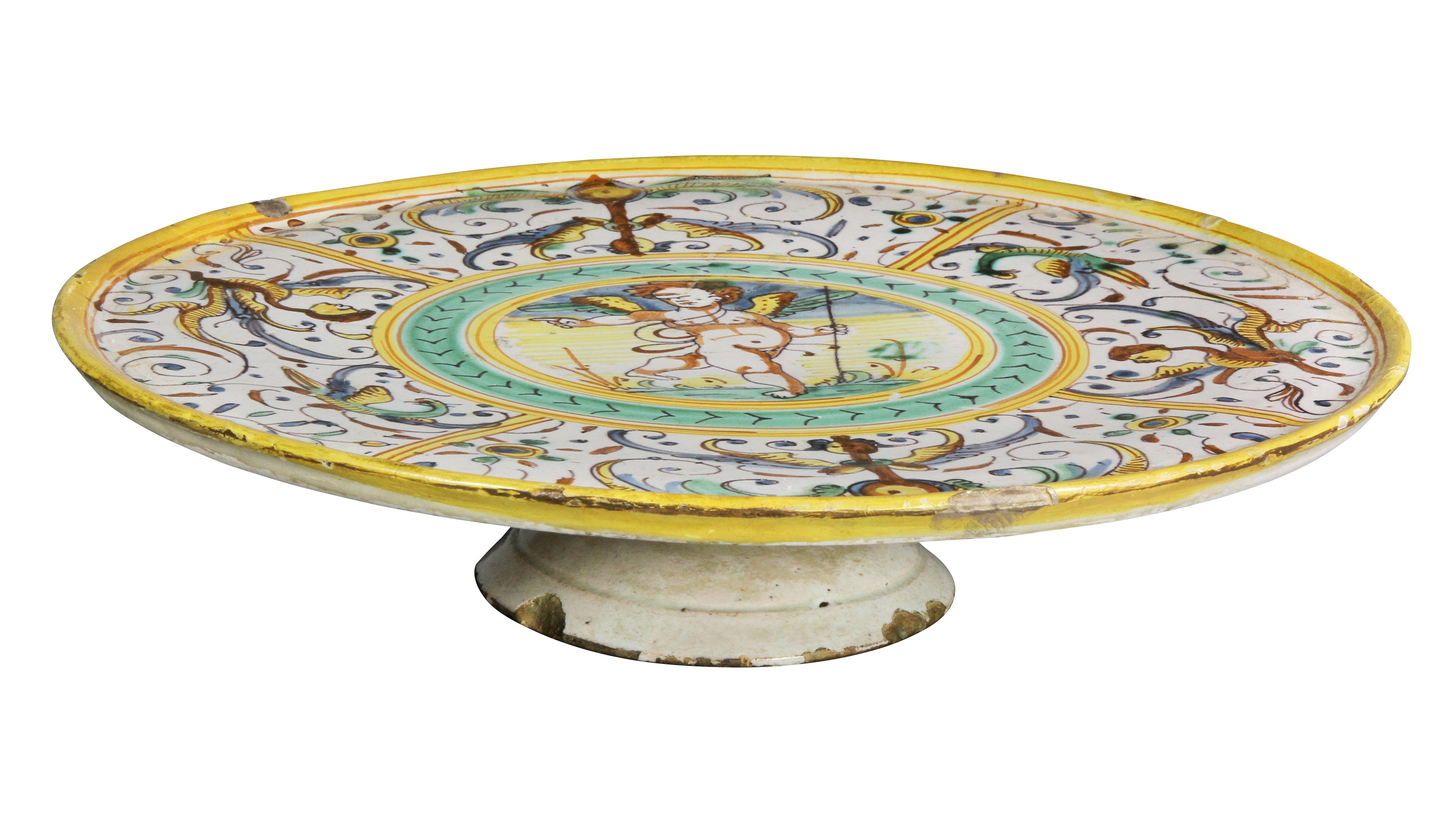 Circular with central cherub holding a staff within a border of winged figures on a circular base.