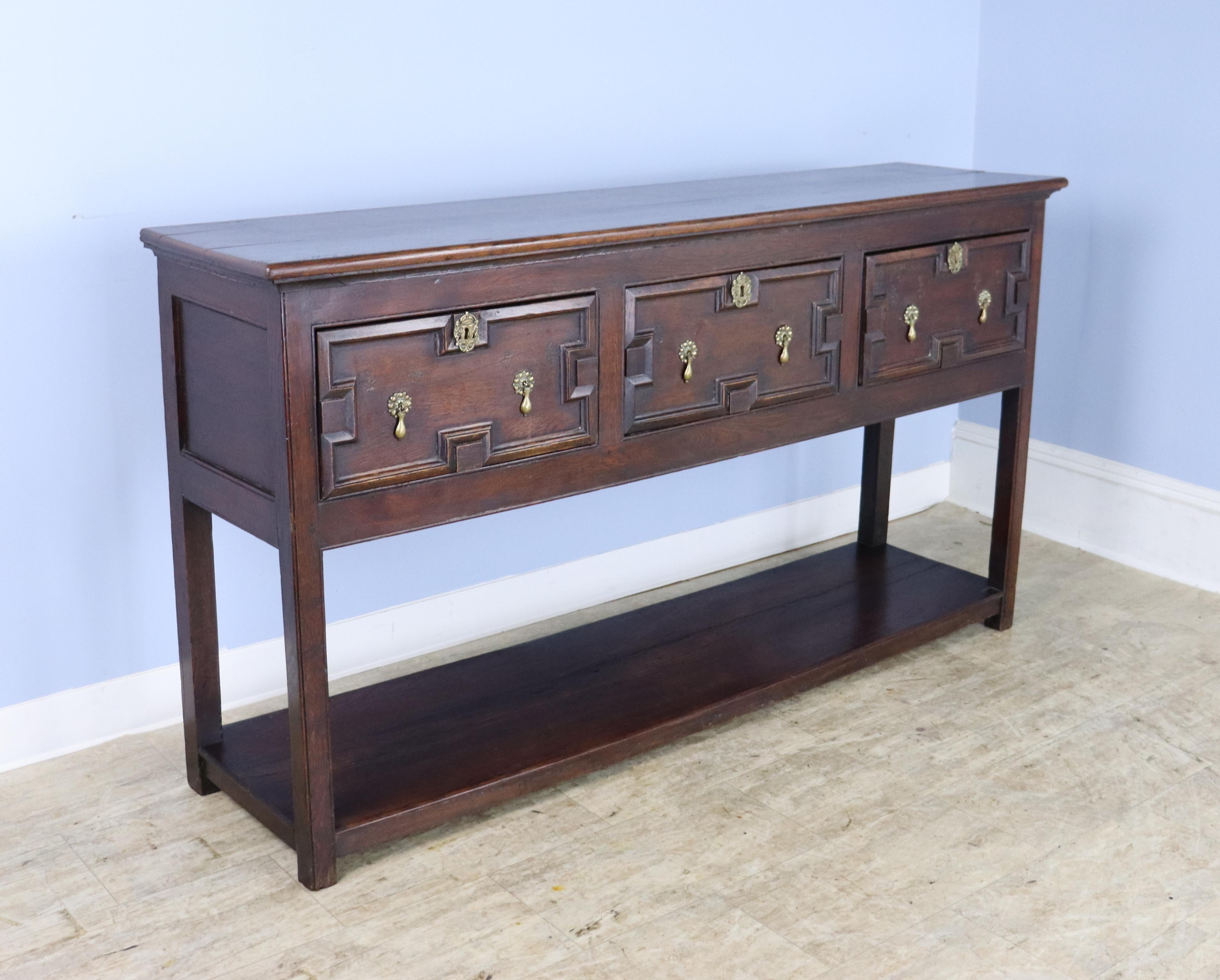 A handsome early dark oak server from the British Jacobean period.  Potbord base with fielded, or carved inset panels on the three drawers, typical of the period.  Original brass teardrop eschutcheons.  The wood has good color and patina and the