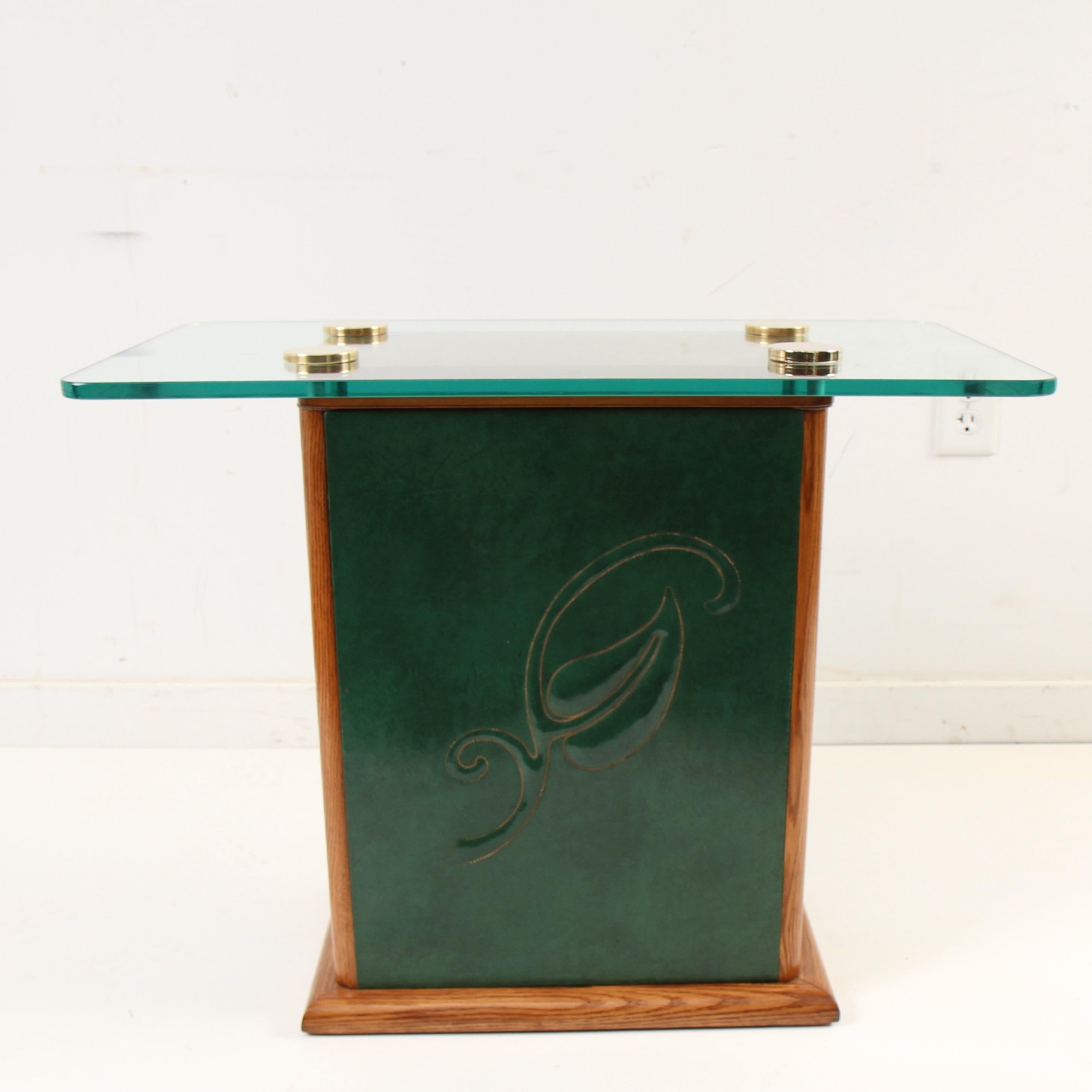 1940s era side or center table with walnut stained oak trim around green, embossed-leather sided base with glass top, secured with solid brass glass tabletop adapters. 

'I CAN DESIGN A CHAIR, A table, a couch, a desk, to fit any curve, crevice or