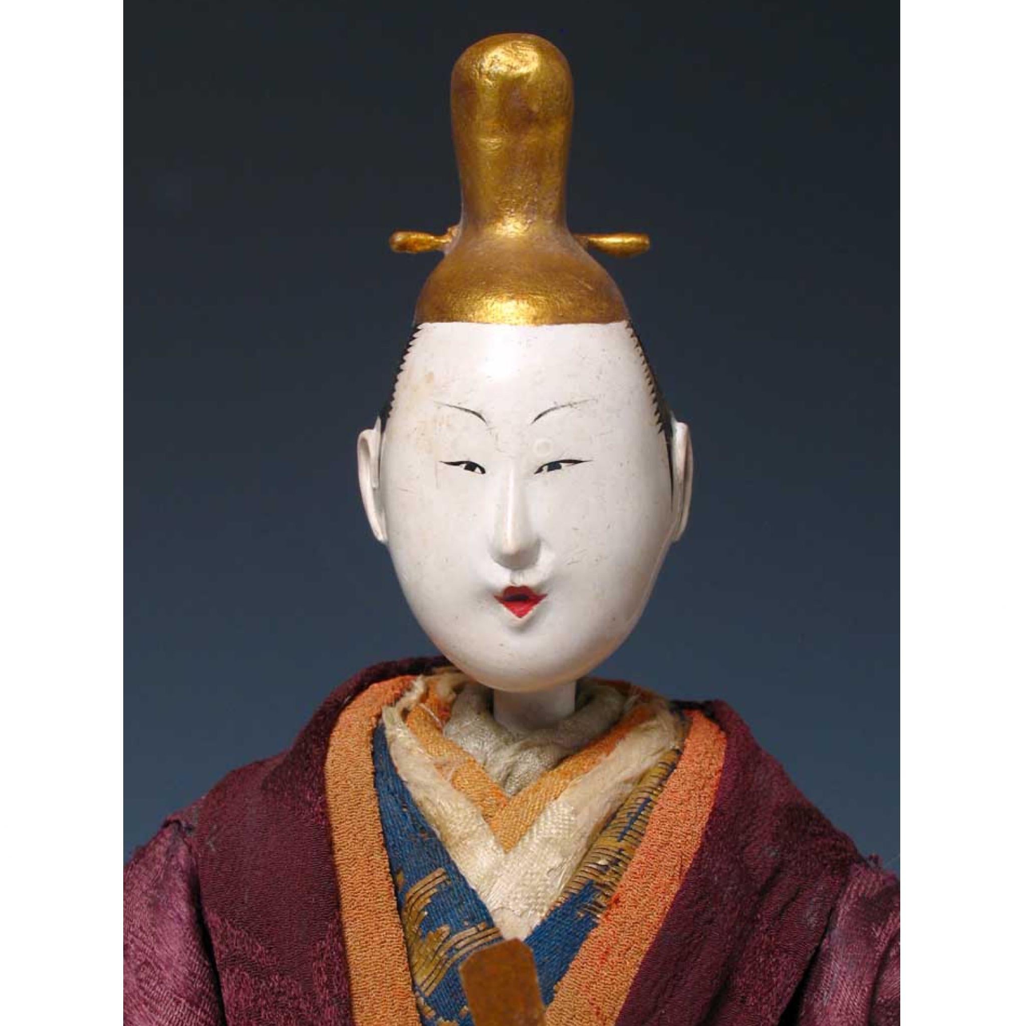 Early Japanese Takeda Ningyo, depicting an actor on stage in the role of an emperor, standing, costumed in silk and kinran brocades holding a paper scepter (shaku), the head carved of wood inclusive of the the peaked gold imperial hat, covered in