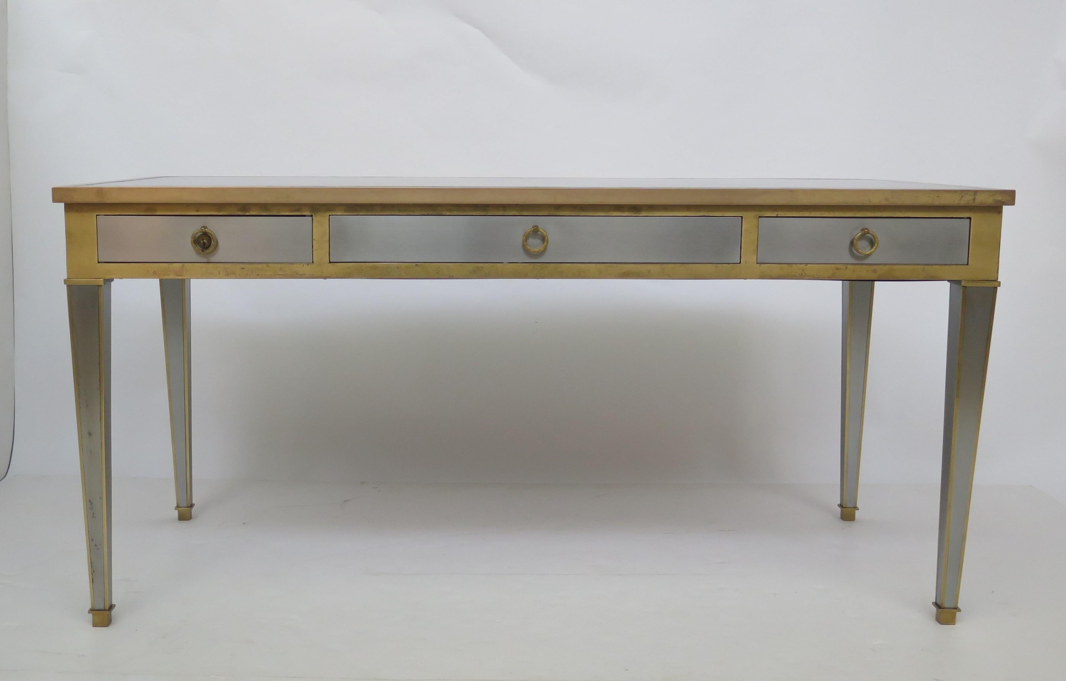 A midcentury Louis XVI inspired bureau plat of stainless steel and gilt bronze with original hand-tooled and gilt-embossed leather top, 3 lined drawers, far left drawer having a lock and key, hardware cast by P.E. Guerin.

Similar to a Vesey