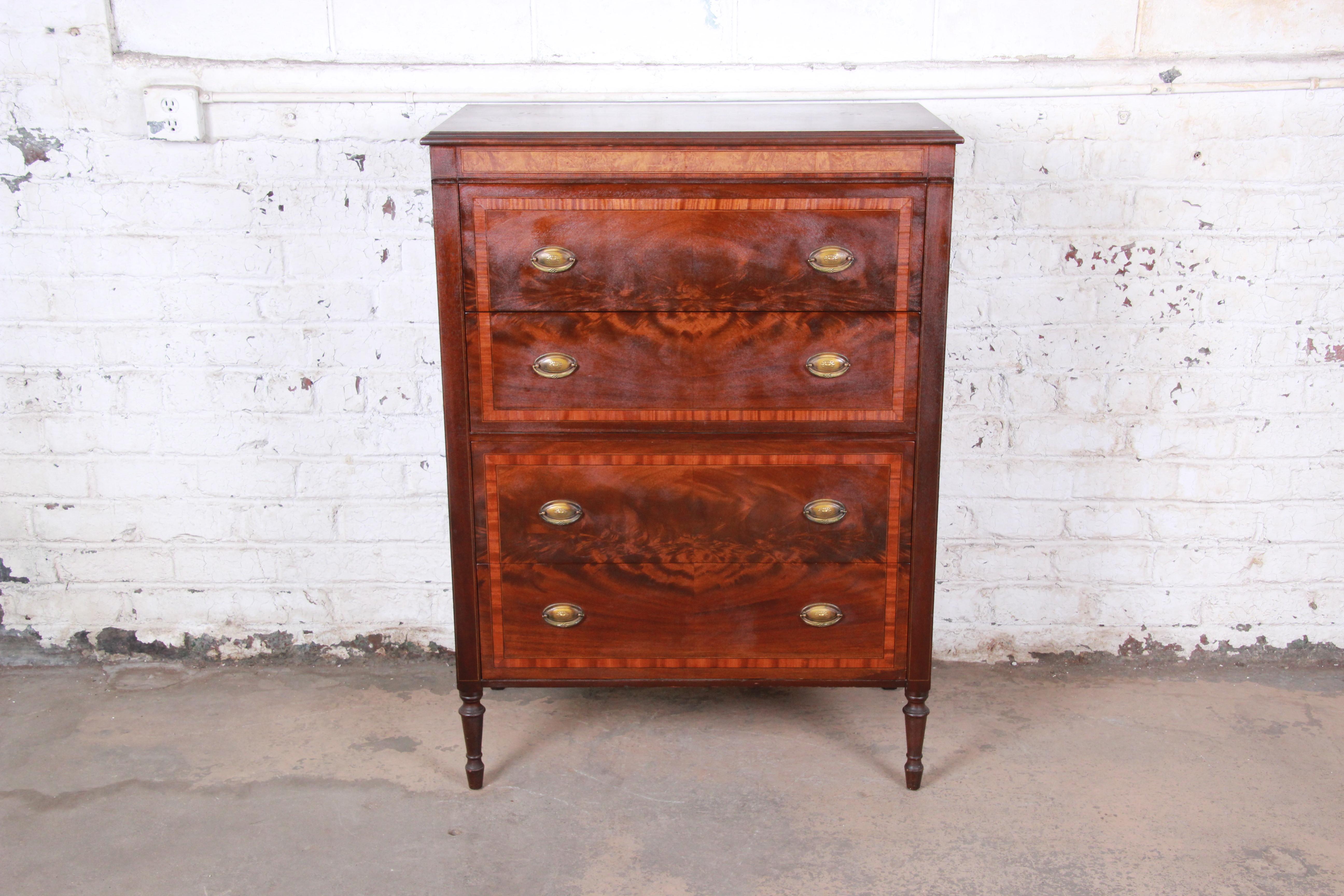 A beautiful and rare early John Widdicomb highboy dresser, circa 1920s. The dresser features gorgeous flame mahogany wood grain with burl wood accents. It offers ample storage, with four deep dovetailed drawers. Brass hardware is original, and the