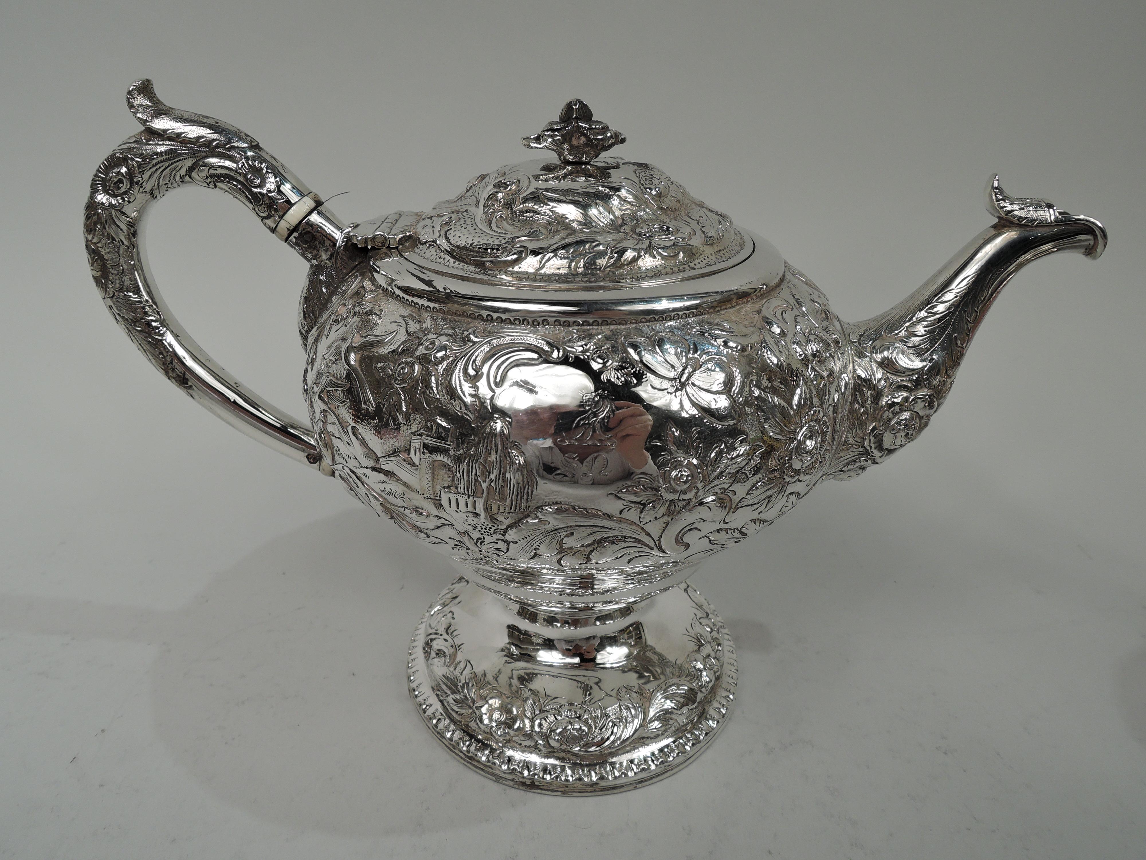 Classical silver teapot. Made by Samuel Kirk in Baltimore in 1828. Ovoid with leaf-capped high-looping handle and leaf-capped tapering spout. Cover hinged and domed with flower finial. Foot domed. Picturesque Classical ruins and hilltop turrets and