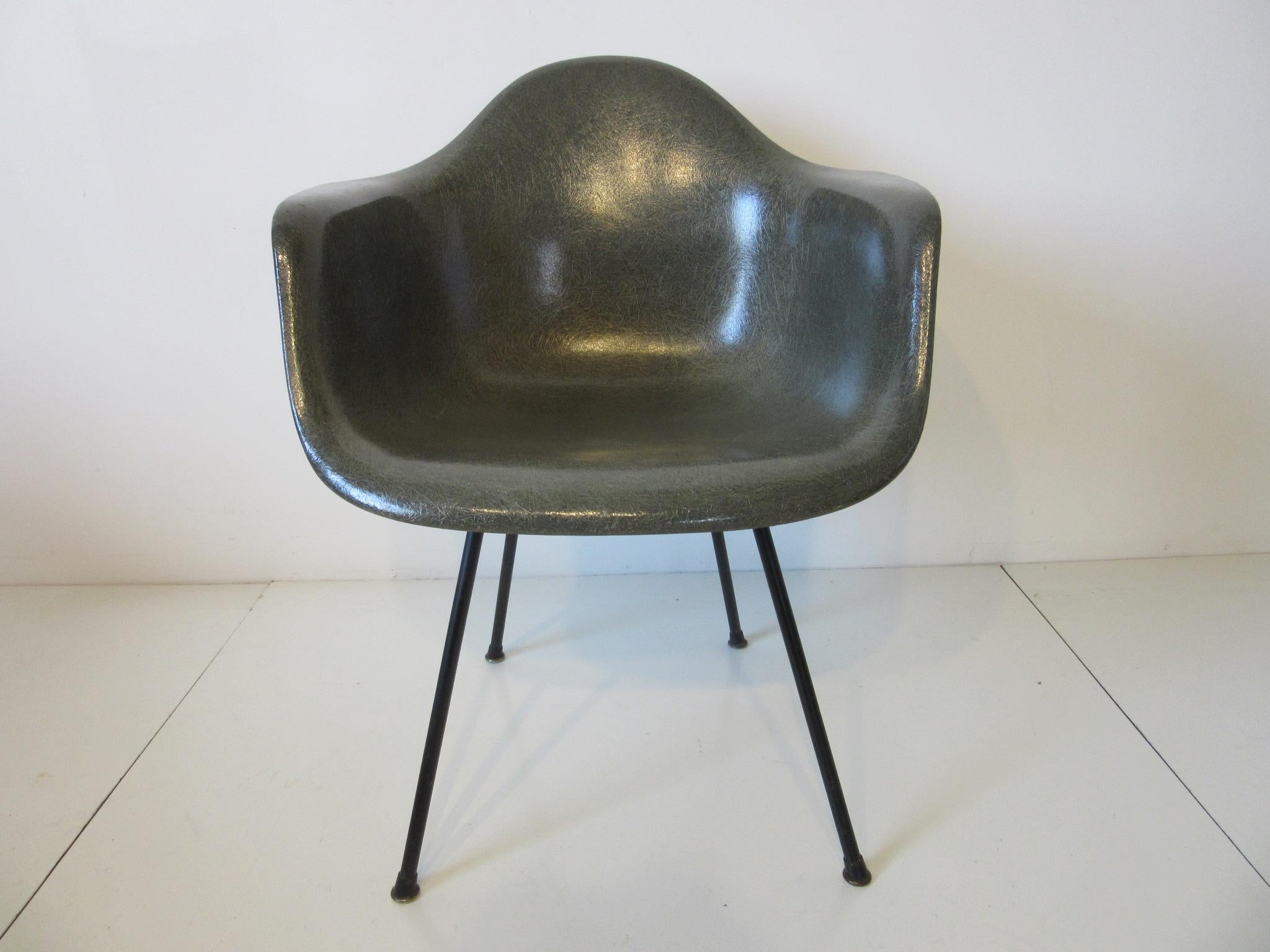 An elephant gray green toned fiberglass armshell chair with satin black iron X-base, rubber and metal boot feet , large early shock mounts and the red second generation decal label with shipped from Venice California. Made by the Herman Miller