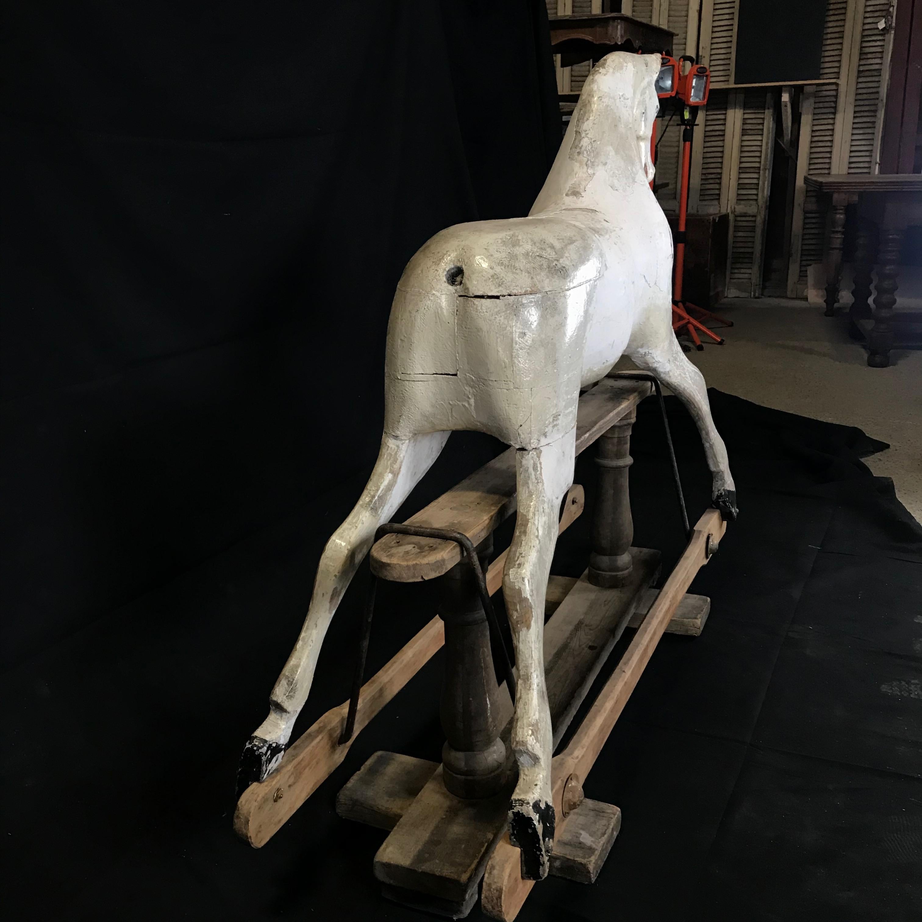 Beautiful early British carousel horse with a stunning whitewashed patina and glass eyes resting on a wooden pedestal support. A sculptural piece of art and eye catching Folk Art focal point. Weathered, small losses and old repairs add to its