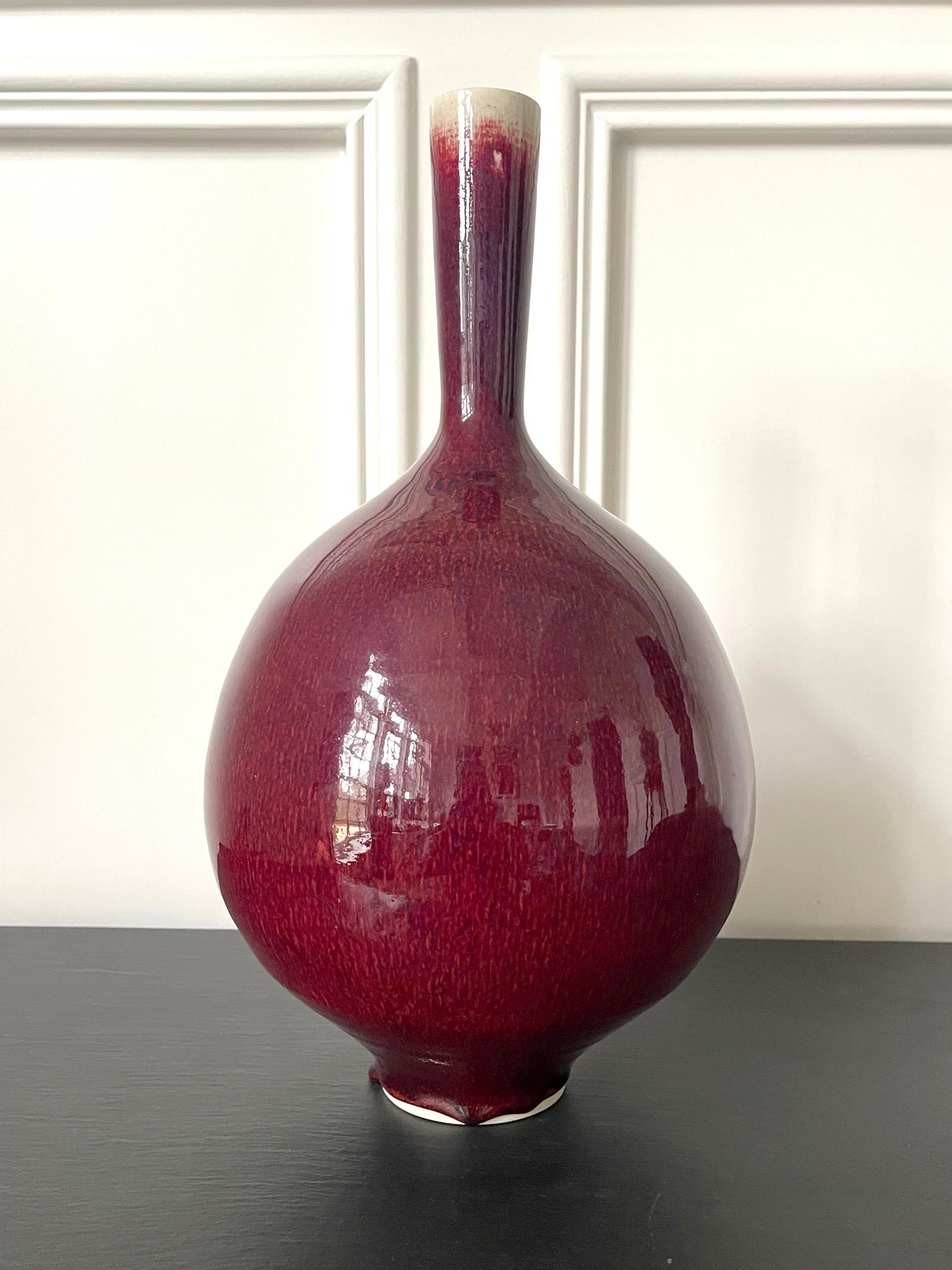 Un vase précoce en céramique à long col, avec une glaçure rouge cuivre brillante, réalisé par le moine potier bénédictin Frère Thomas Bezanson (1929-2007). La forme minimaliste et harmonieuse, avec un corps bulbeux, est indubitablement inspirée de