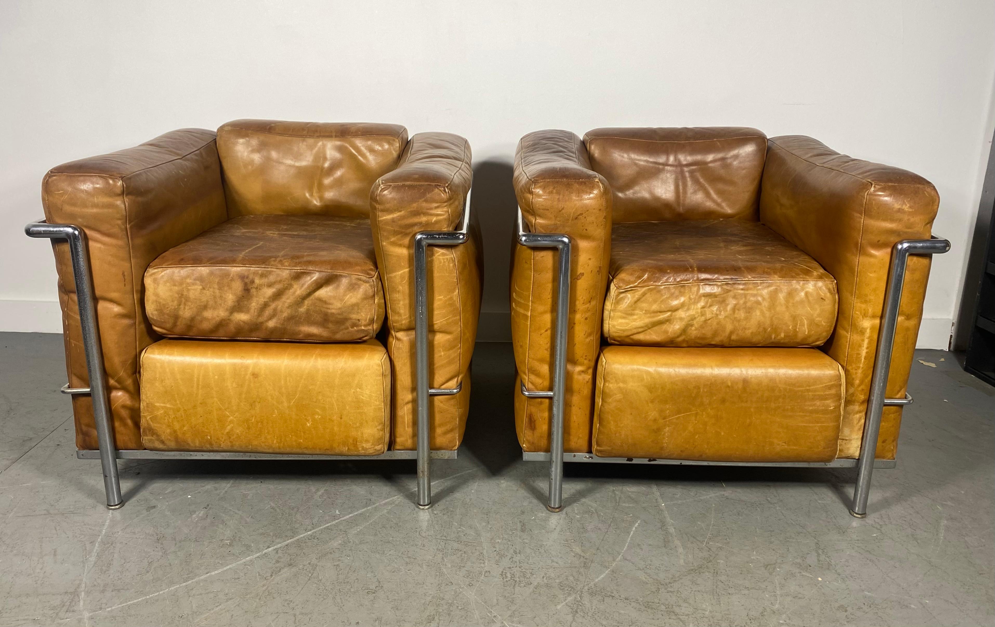 Superfrühes Paar von  LC2 Petite Modele Sessel Entworfen von Le Corbusier, Pierre Jeanneret, Charlotte Perriand, hergestellt in Italien mit original braunen Lederkissen und Chromgestell. Die Stühle sind in gutem Zustand insgesamt, Truely