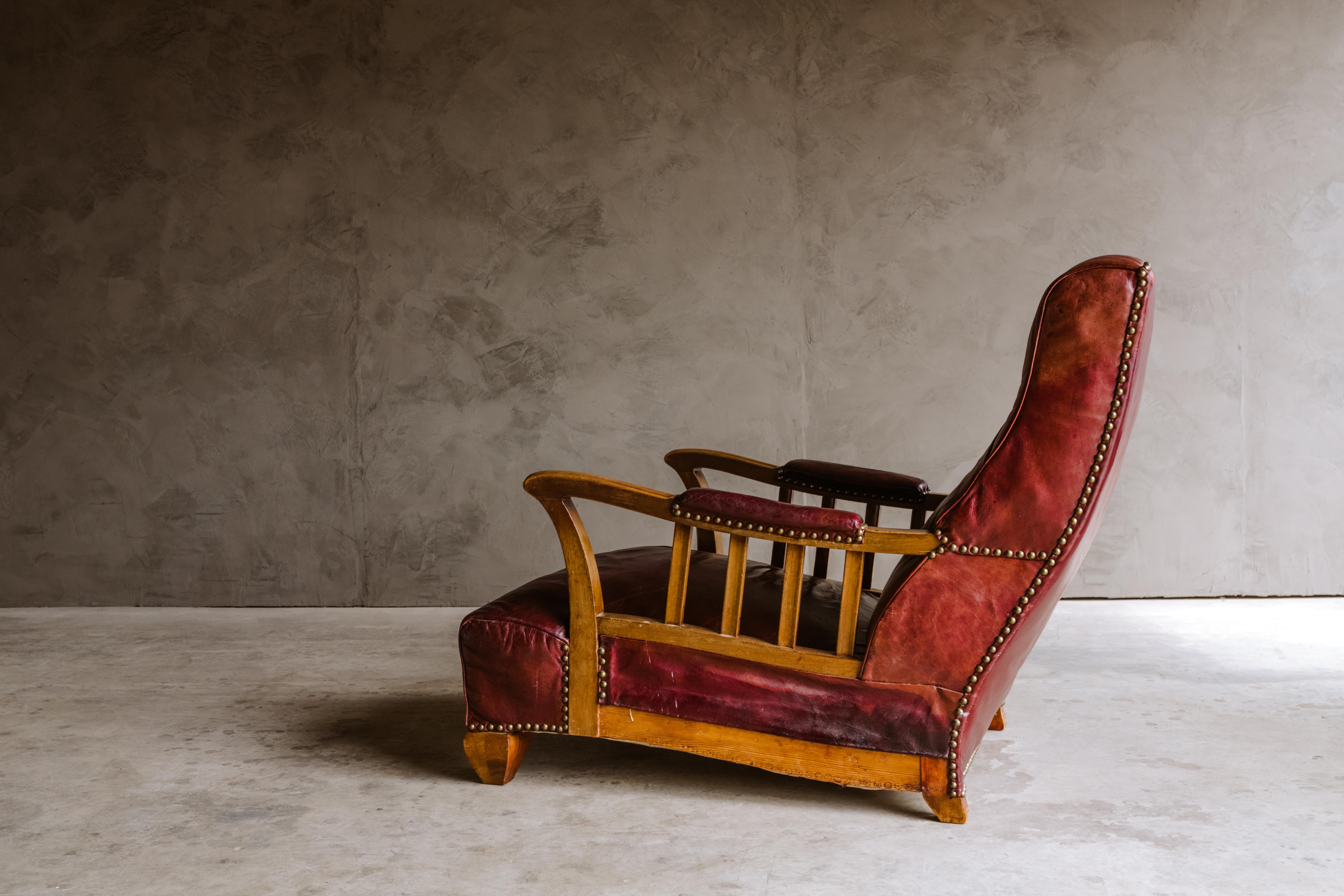 Early leather lounge chair from Sweden, 1940s. Original red leather upholstery with solid oak arms. Nice patina and wear.