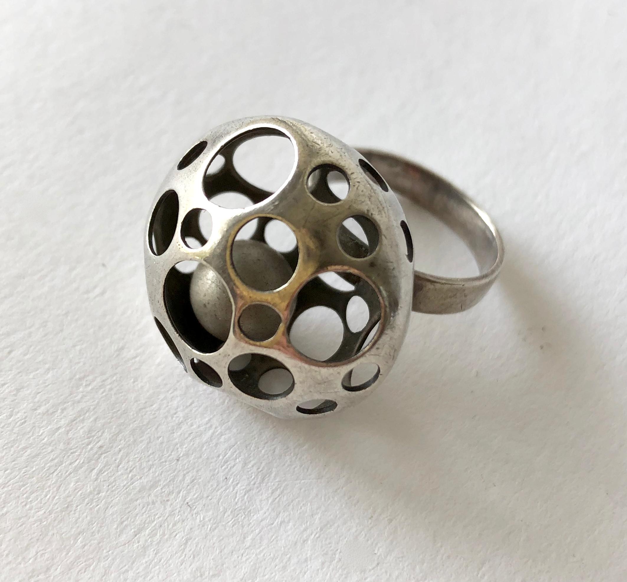 Perforated sterling silver ring containing a kinetic ball within created by Liisa Vitali of Finland.  Ring is a finger size 6 3/4 and is signed on the shank with Finnish hallmarks, M7 (1965).  In very good vintage condition and retains original