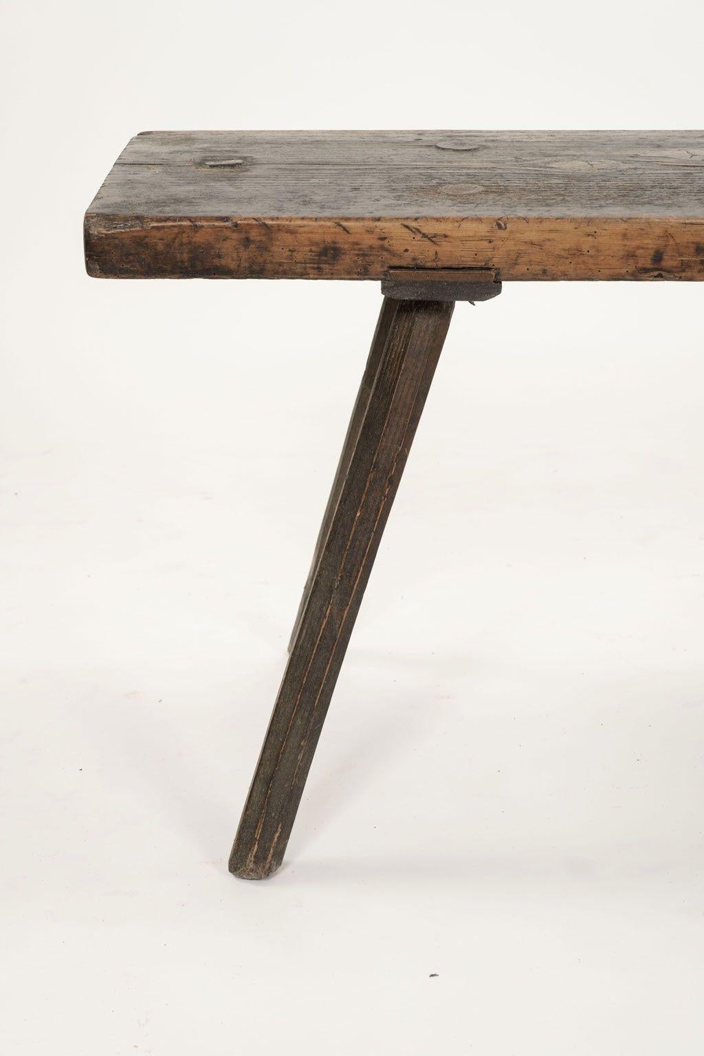 Early long pine bench circa 1710-1739: single thick plank of pine raised upon four splayed simple carved legs. Early finish. Sturdy, stable pegged construction.