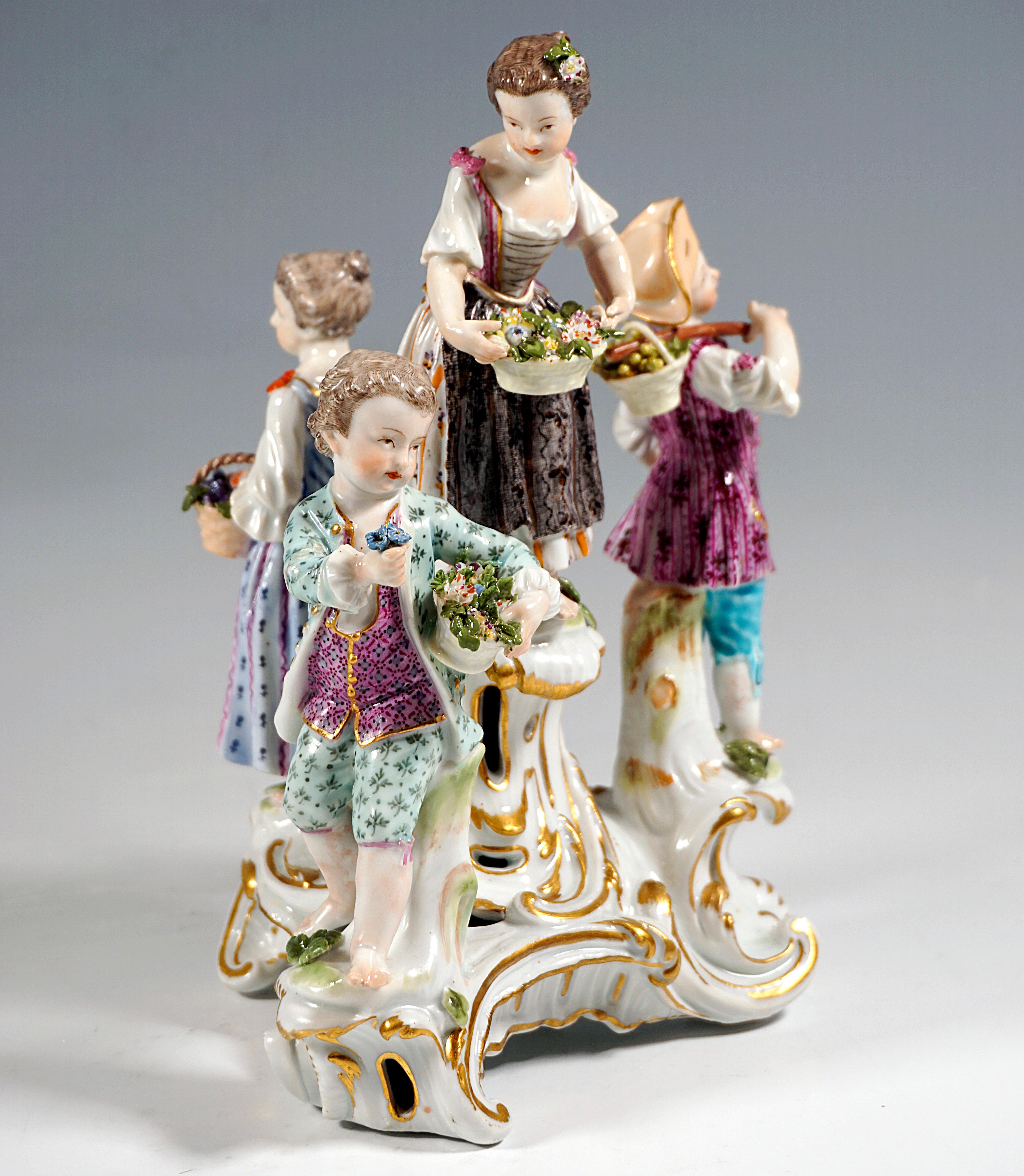 Meissen porcelain group from the time of origin:
Four children in festive, rural rococo clothing on a three-part rocaille base: on the central raised pedestal a girl with a basket of flowers, leaning towards the boy to his right on a lower step,