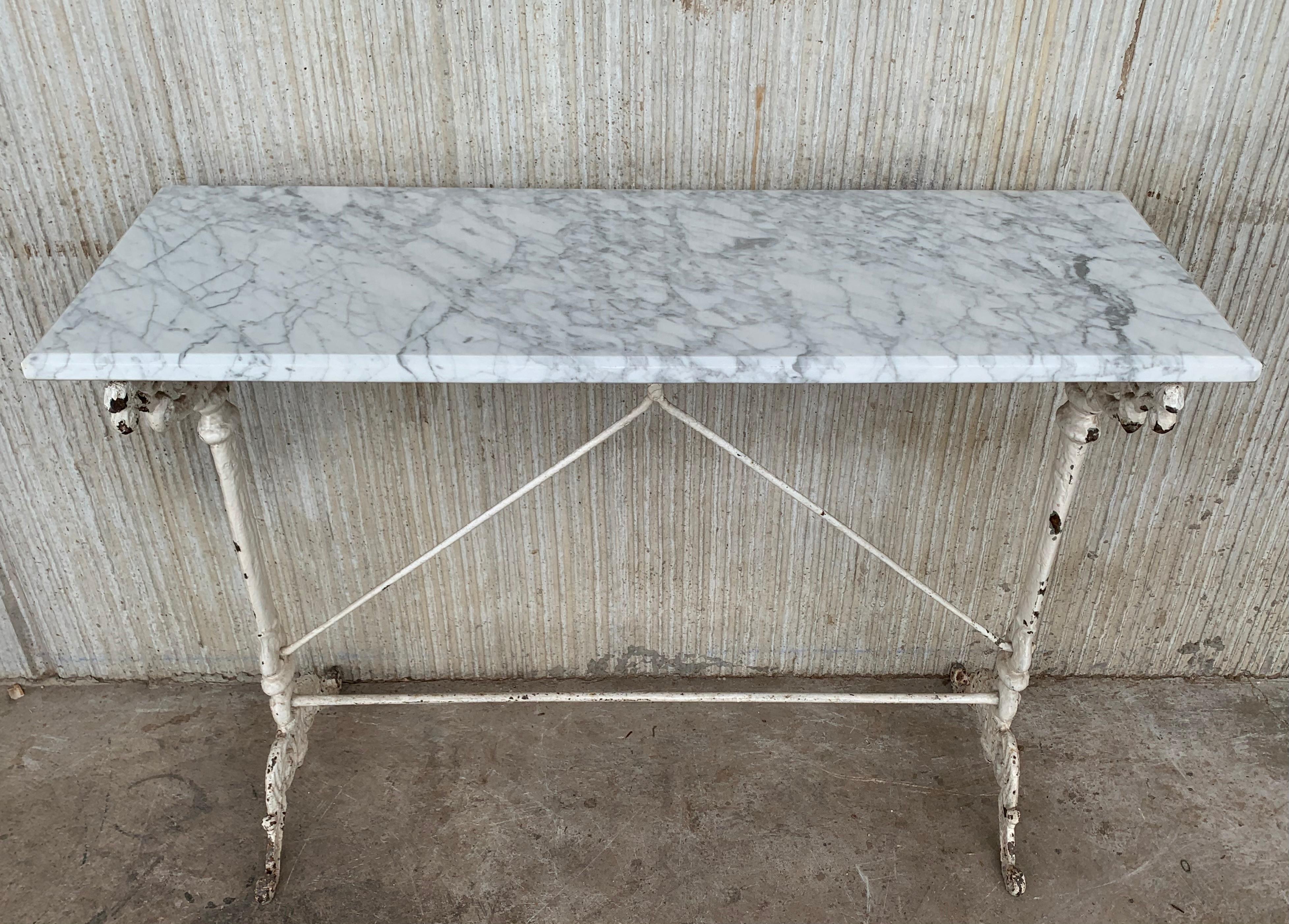 From France, this charming rectangular bistro table has a marble top. The boards are thick, and they have a curved molded surround. The iron pedestal legs has a worn painted finish in the same tones, and it is decorated with motifs of fluting,