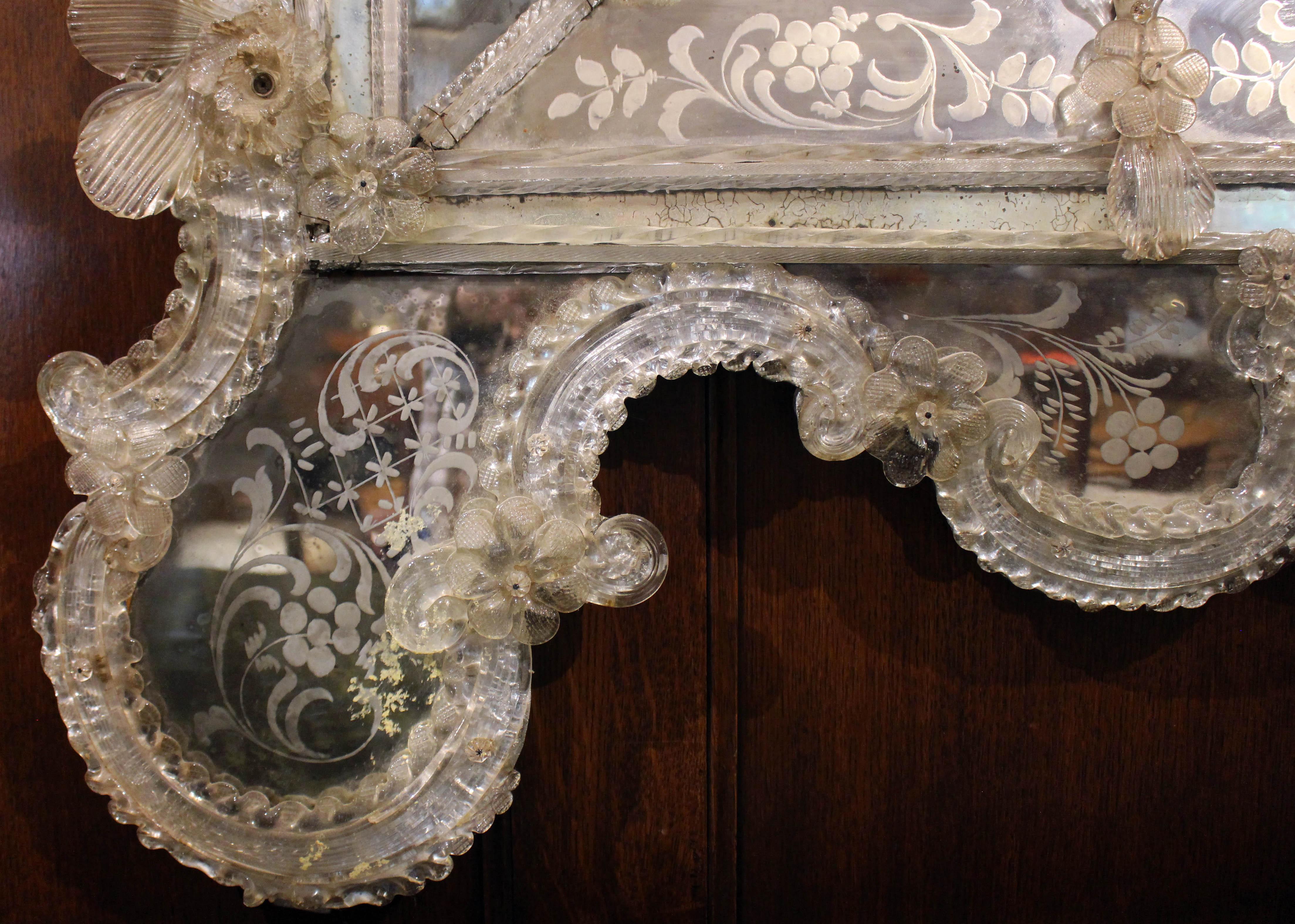 An important Venetian mirror, Baroque-Rococo transitional revival. The basic rectangular form with corner panels is Baroque, while the asymmetrical crest displays Rococo at its best. Mirror paneled in etched & engraved mirrors festooned with blown