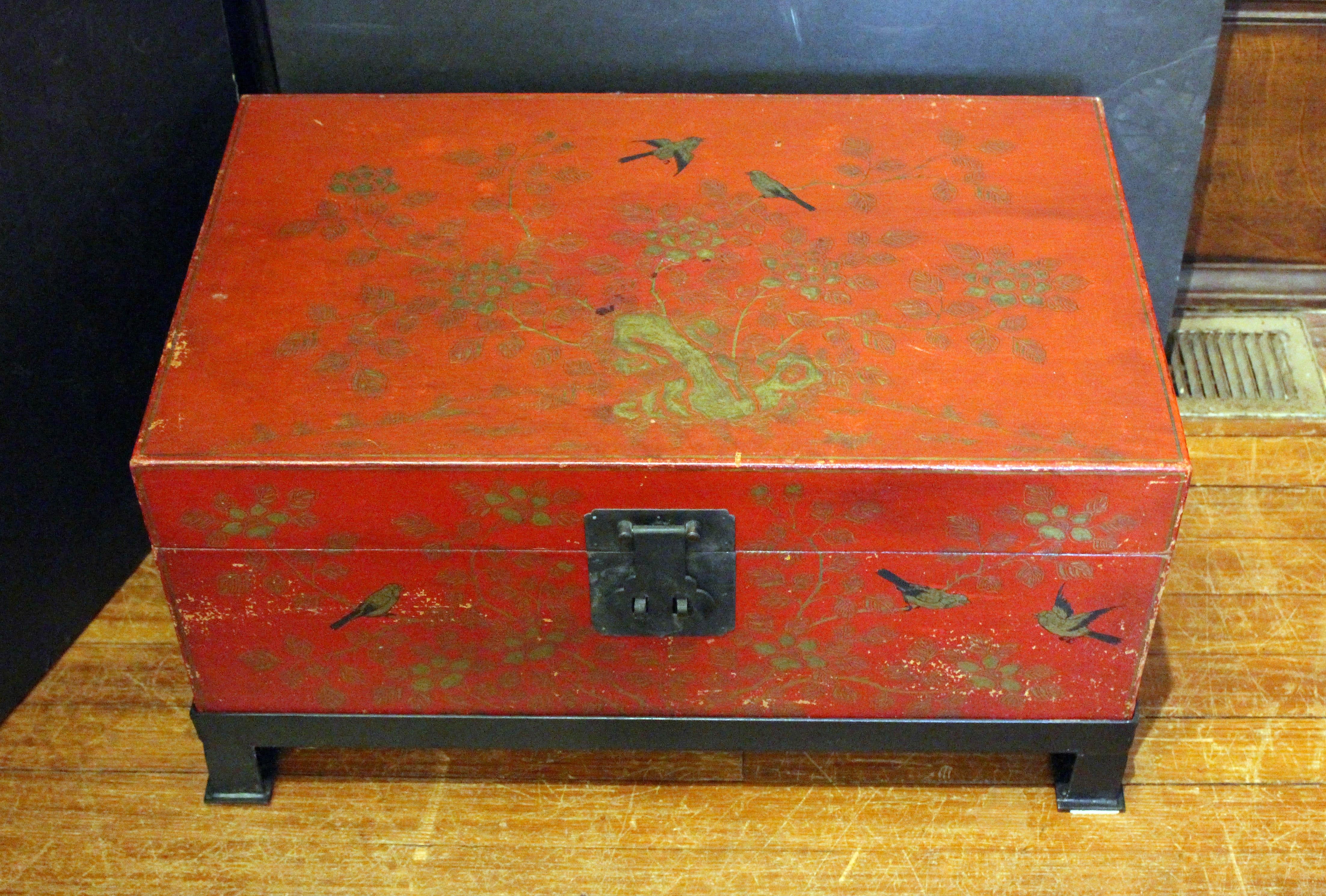 Early-mid 20th century Chinese red & gilt coffee table trunk on custom iron stand. Parchment leather applied to wood - various losses & scuffs commensurate with material & age. Decorated on 3 sides with rocky outcroppings with trees & birds. Iron