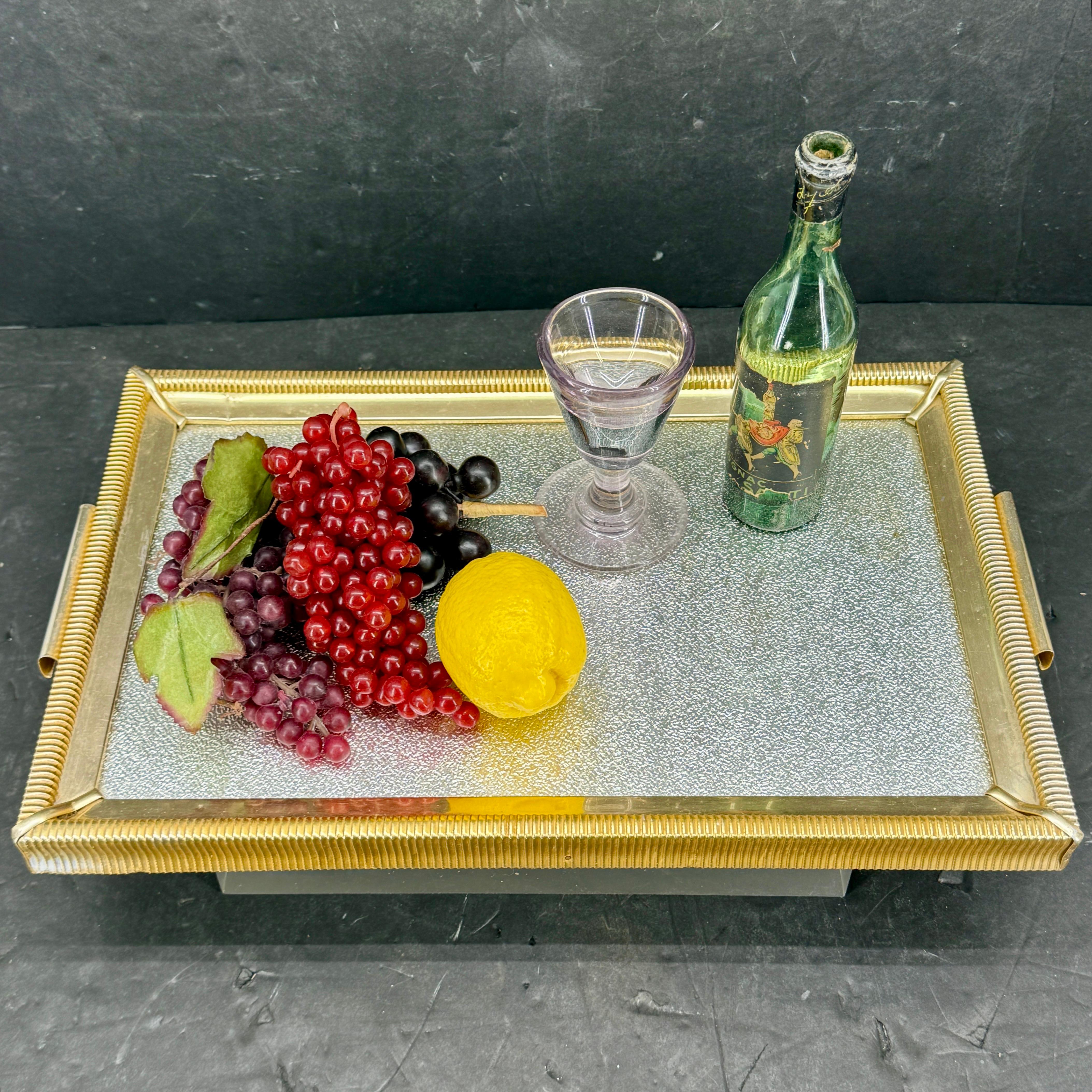 Bandeja rectangular de latón, aluminio y madera de la Italia de los años 1930-1940. La bandeja con asas tiene un borde de latón con un centro de aluminio plateado texturizado. Vemos esta bandeja utilizándose funcionalmente en una mesa de centro de