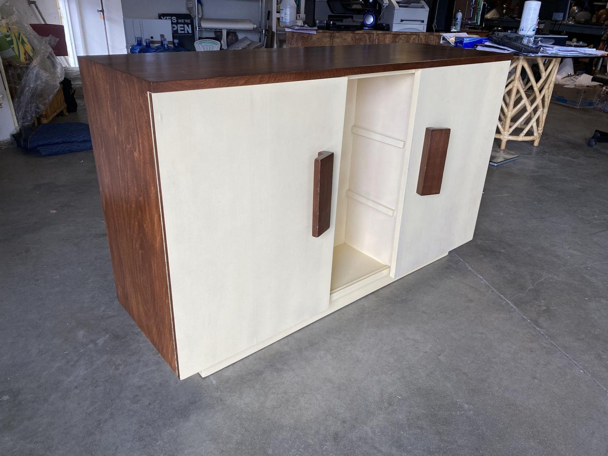 Elegant walnut buffet cabinet designed by Paul Frankl for The Johnson Furniture Company, American, circa 1940. This cabinet has been refinished in a slight red hue on the cabinet case with off-white doors.
The cabinet features 4 pull shelves on