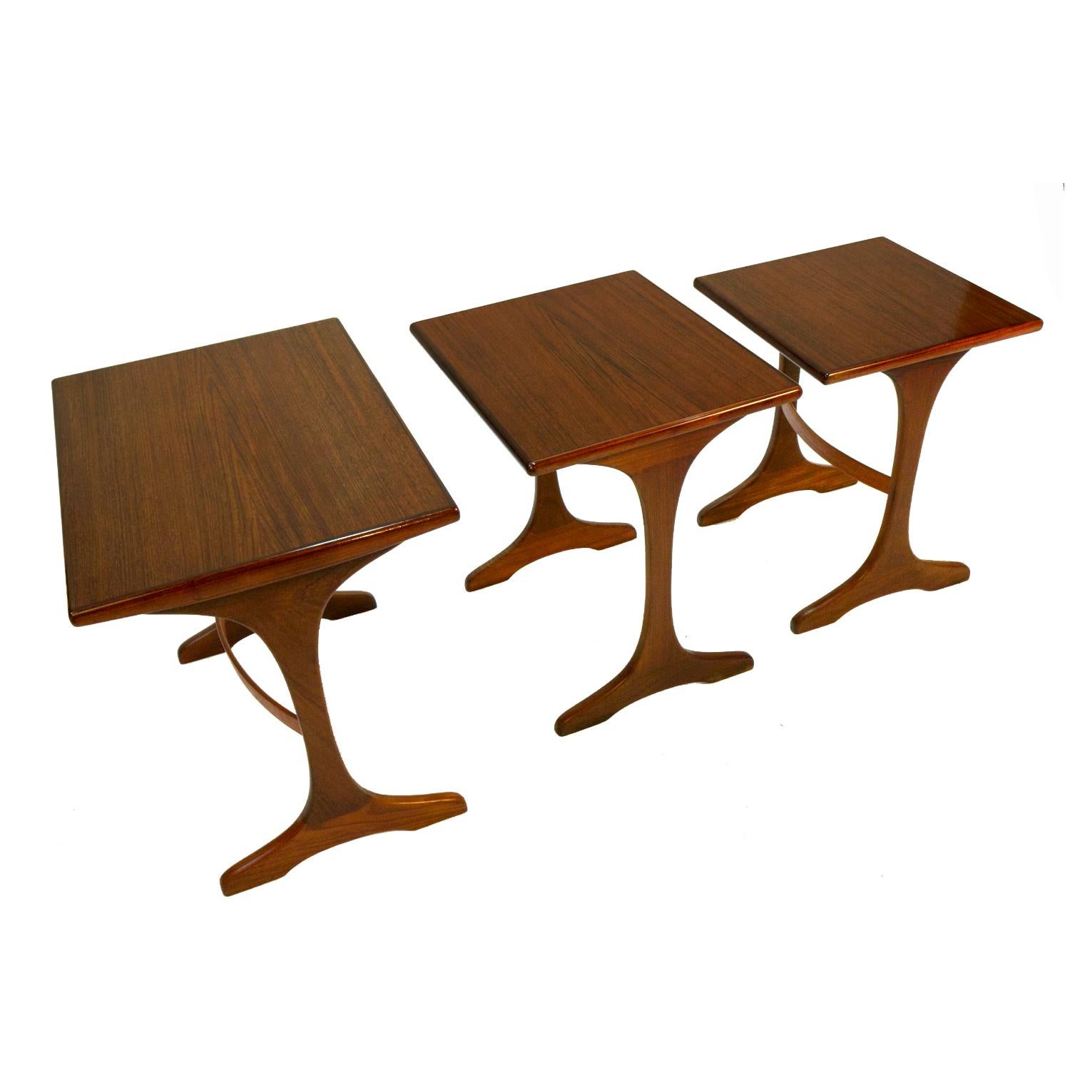 Set of three refinished Mid-Century Modern teak nesting tables by G Plan. Made in England. We love these tables for their unique design. The set of three graduates in size, allowing the smaller tables to easily stow beneath the large table. Over