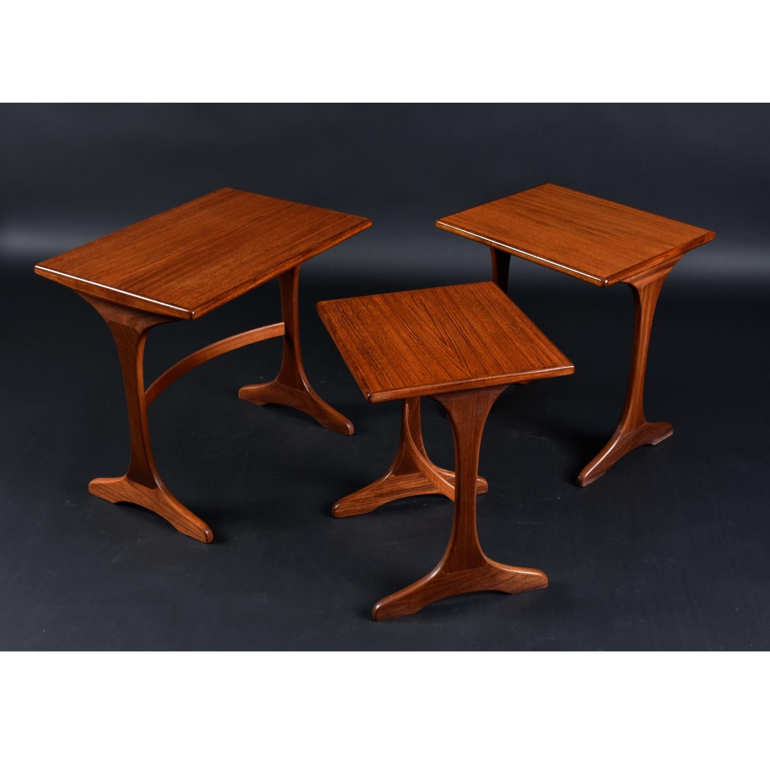Set of three refinished Mid-Century Modern teak nesting tables by G Plan. Made in England. We love these tables for their unique design. The set of three graduates in size, allowing the smaller tables to easily stow beneath the large table. Over