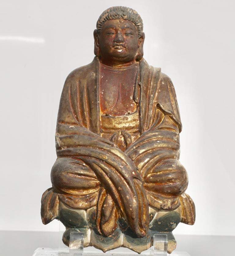 A very fine late Yuan to early Ming Chinese terracotta gilt and polychrome painted Buddha figure, he is dressed in thick robes, his hair arranged in typical early song or Yuan dynasty style and he is sitting on a colorful blue lotus flower. This