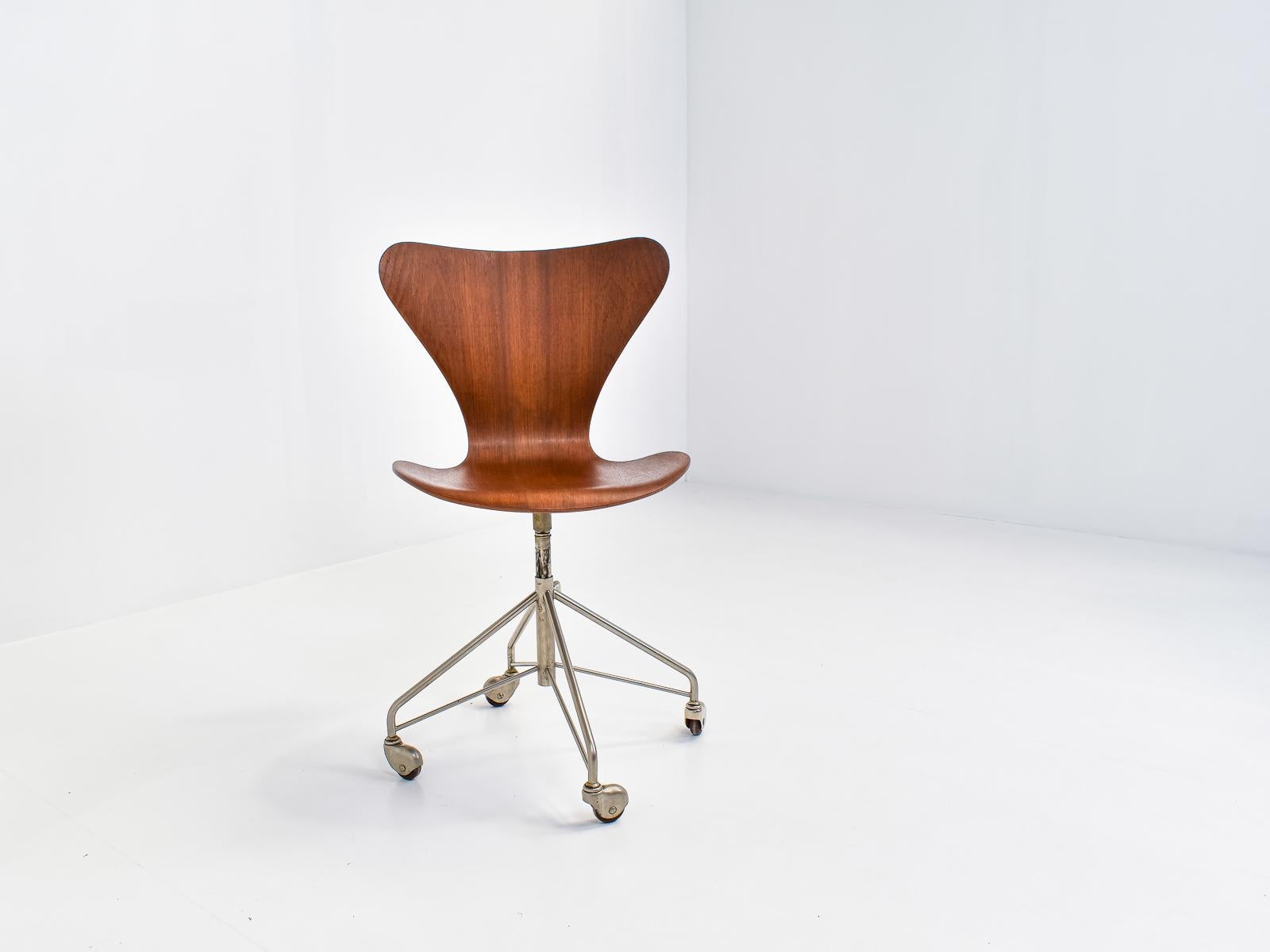 Early model in excellent original condition. Series 7 designed by Arne Jacobsen in 1955. 
Four wheel base (1st edition) in chrome plated steel, seat in teak veneer. 

Adjustable seat. Seat height (44-56cm).
 