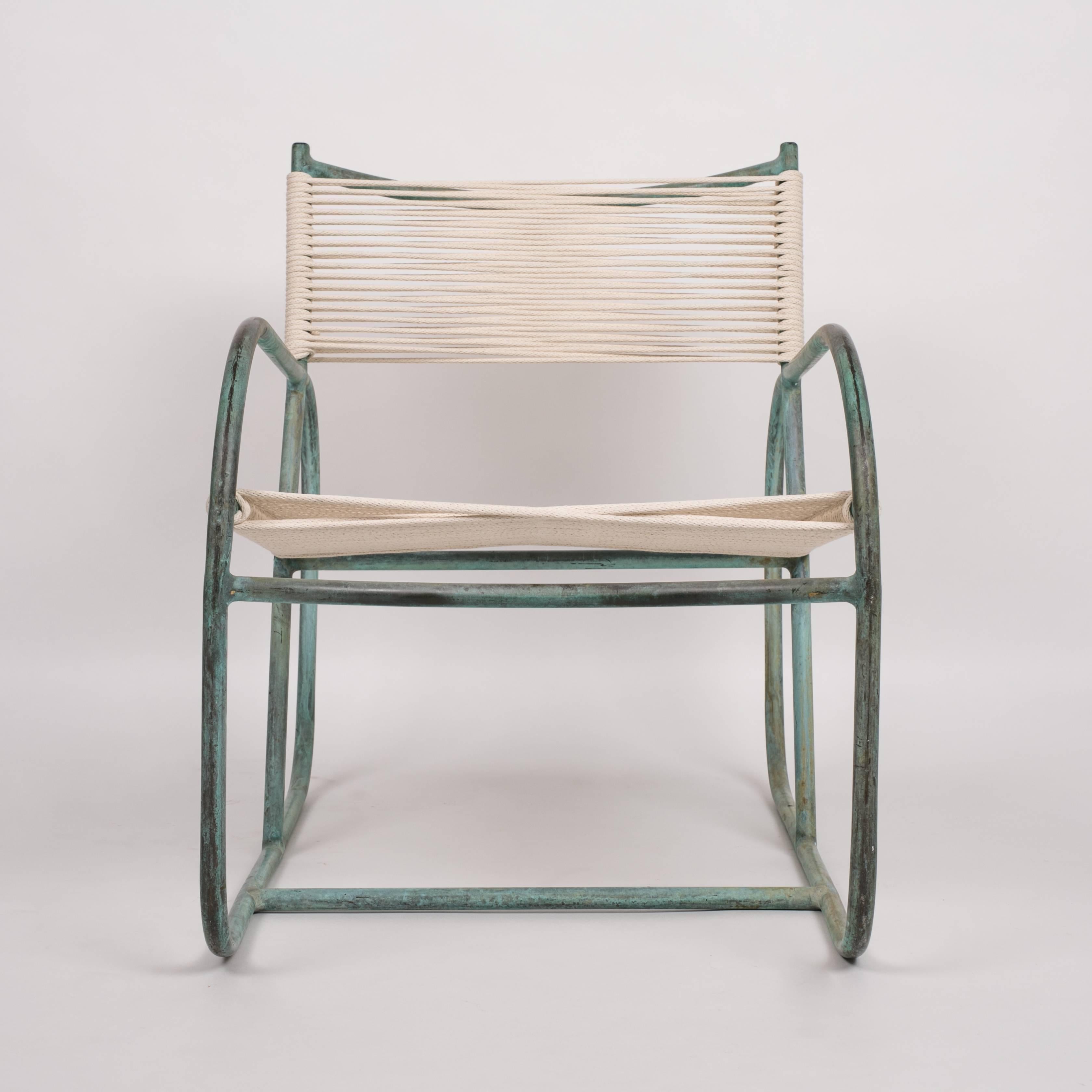 A 1940s Walter Lamb lounge chair predating his partnership with Brown Jordan, this piece has an angled backrest bisecting two rounded runner arms. The patinated frame in tubular bronze is strung with cotton-nylon sail cord, woven to form a seat and