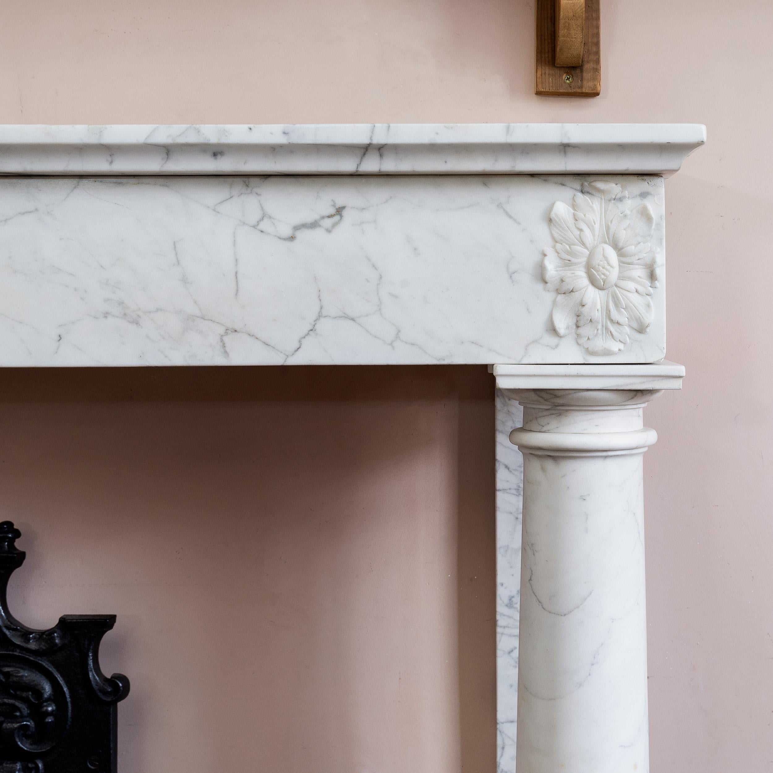 An early 19th century French Empire fireplace, the plain frieze with carved foliate paterae supported by disengaged Tuscan columns and pilasters, in Carrara marble, hearth not included (available separately).

A handsome, understated and stylish