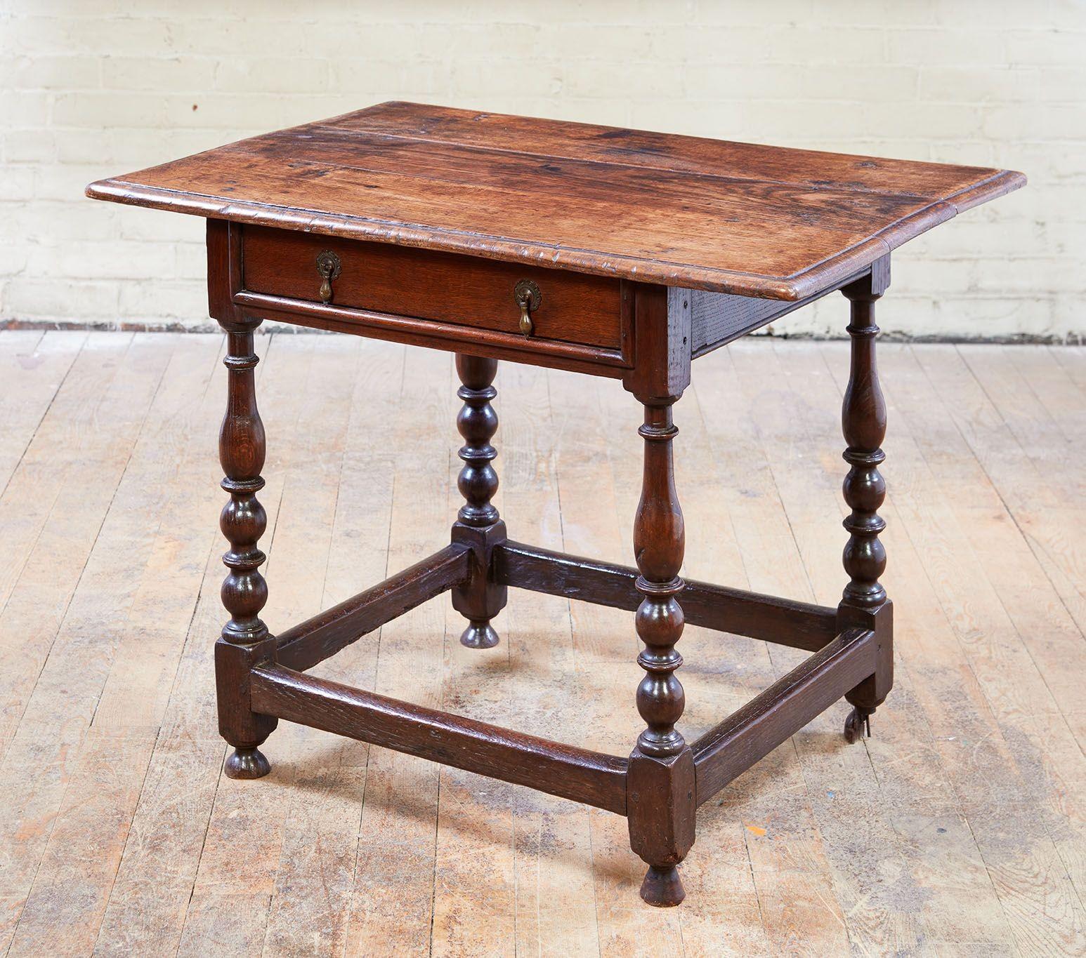An early English oak side table with lovely well-patinated three plank molded top with flying overhangs to sides above single drawer with two drop pulls surrounded by edge molding, over boldly turned legs joined by rectangular section box stretcher