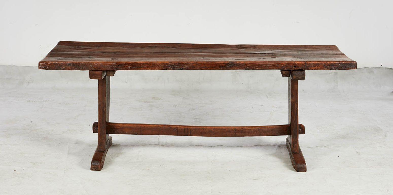 An early trestle table with a thick two plank top retaining its historic surface supported on two wide trestles with sled feet, joined by a low stretcher. Good color and bearing a carved name 