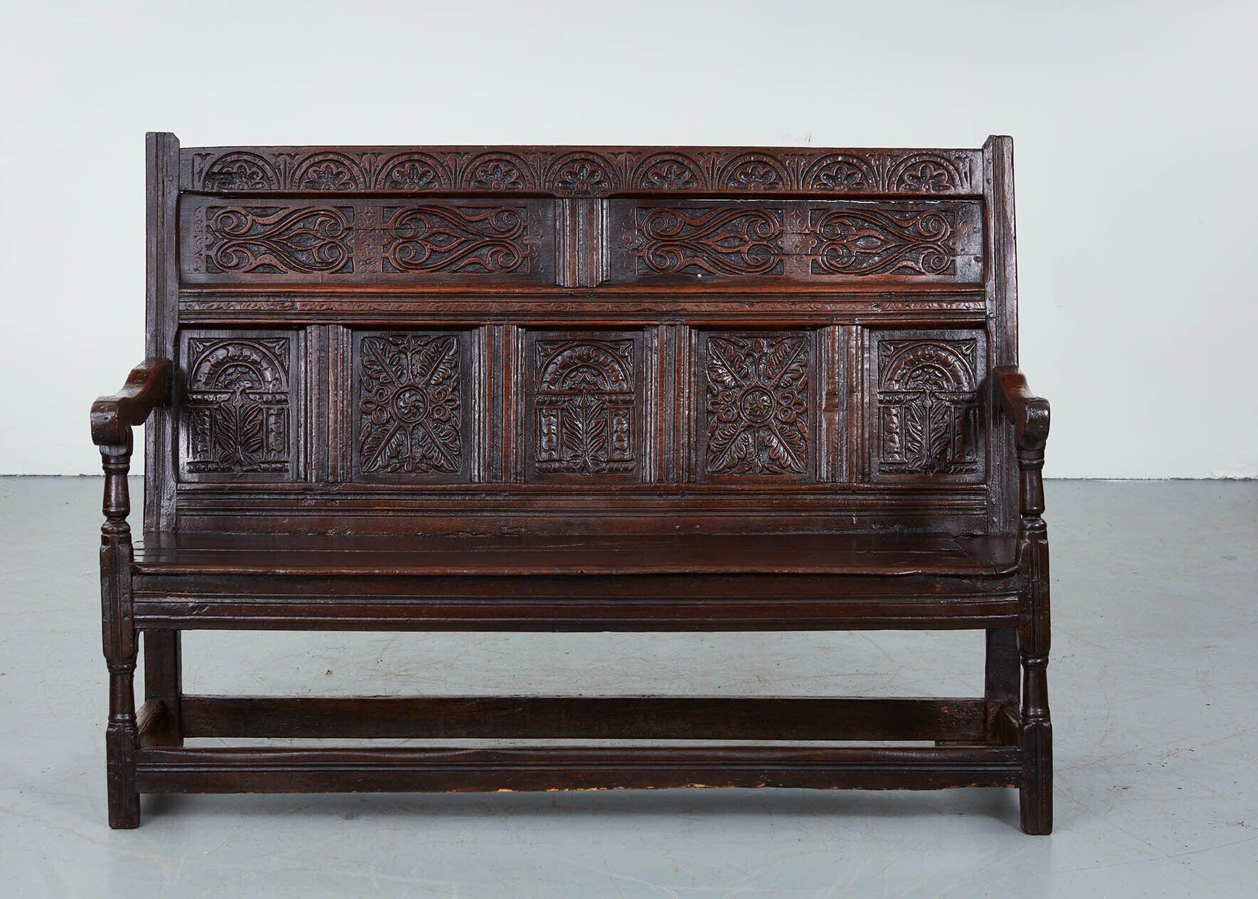 An English 17th century oak bench or settle with tall wainscot back suberbly hand-carved with profuse arched and foliate decoration in two tiers of four over five paneled sections on plank seat with shaped arms and turned arm support and front legs,