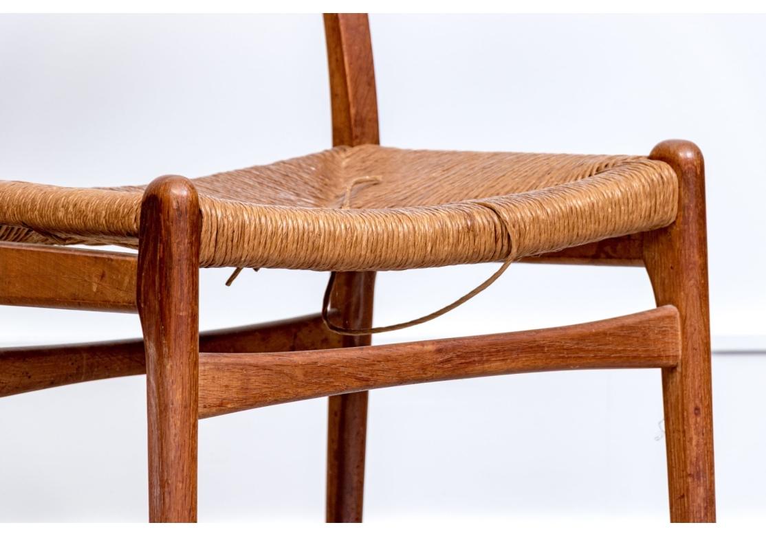 Classic Danish Mid Century chairs designed by Hans Wegner. The chairs in a sophisticated mix of teak and oak with rush seats and having the cruciform pegs on the backs. This is an older pair with some edge nicks and some breaks and losses to the