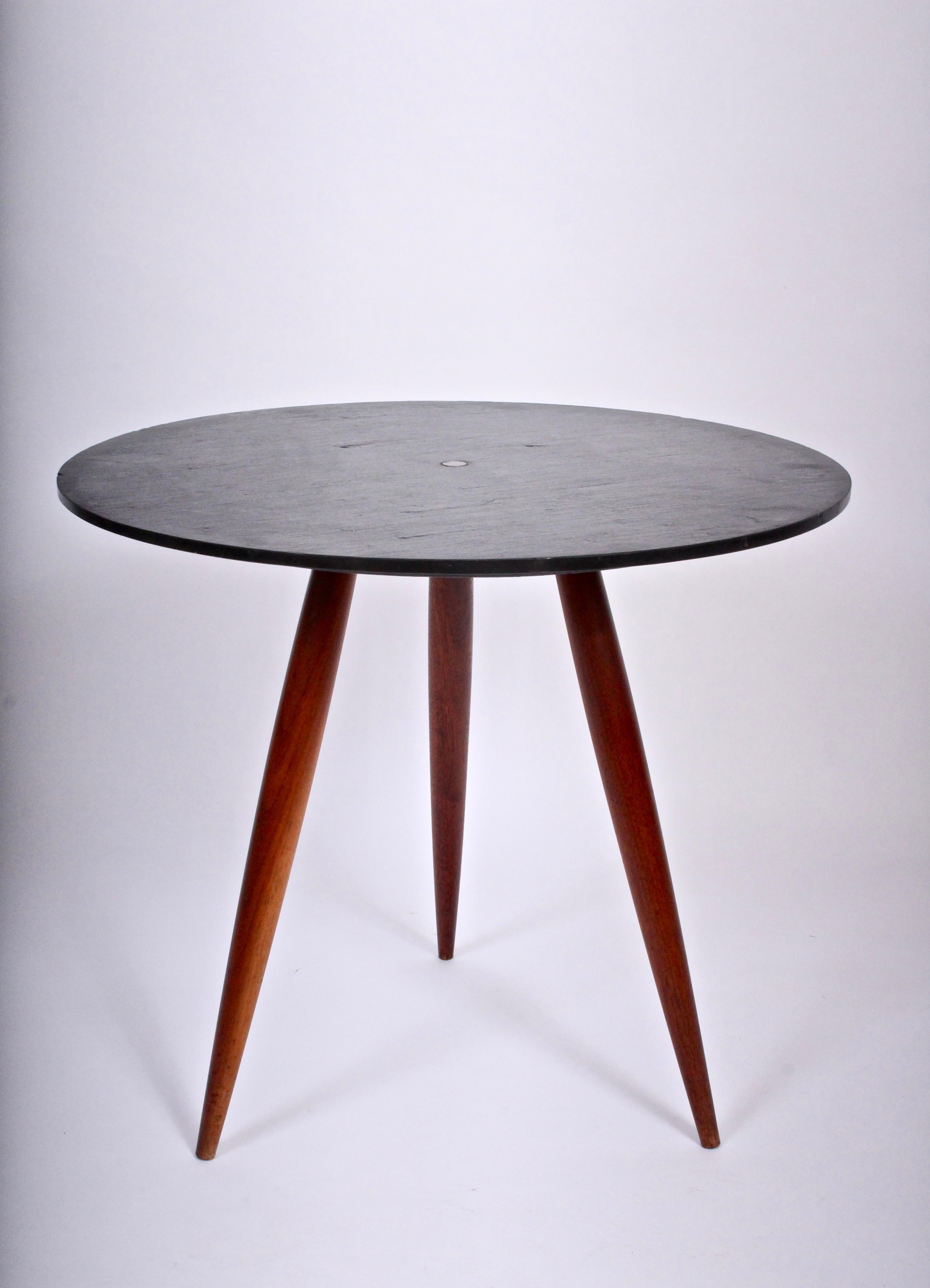 Phillip Lloyd Powell circular walnut tri leg table with dark natural slate surface. Featuring three turned walnut legs, round natural cleft charcoal gray slate table top, classic round flat center brass pin. Balanced. Modernist. Rarity.  Unmarked.