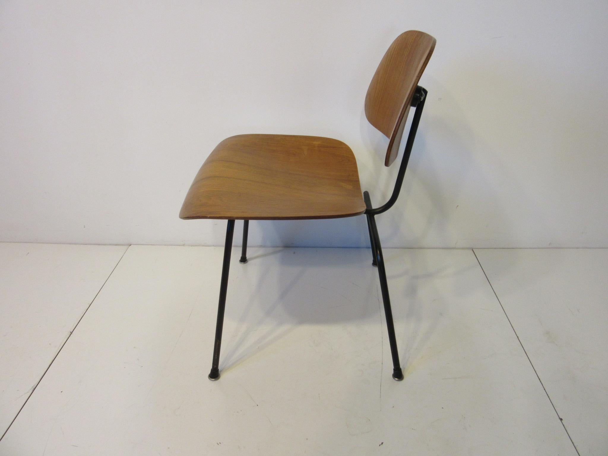 An early production DCM molded well grained oak wood side chair with factory black metal frame and rubber metal boot styled feet. To the seat bottom is a remnant of the early label, pencil mark 49 and production shock mount placement marks and