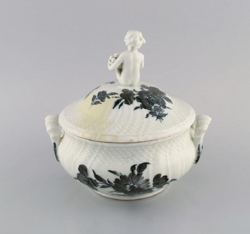Early Royal Copenhagen blue flower curved lidded tureen in porcelain with hand-painted flowers. 
Lid modelled with fruit-eating putto. Approx. 1820
Measures: 21 x 20 cm.
Restored lid and a small chip on one handle.
Stamped.