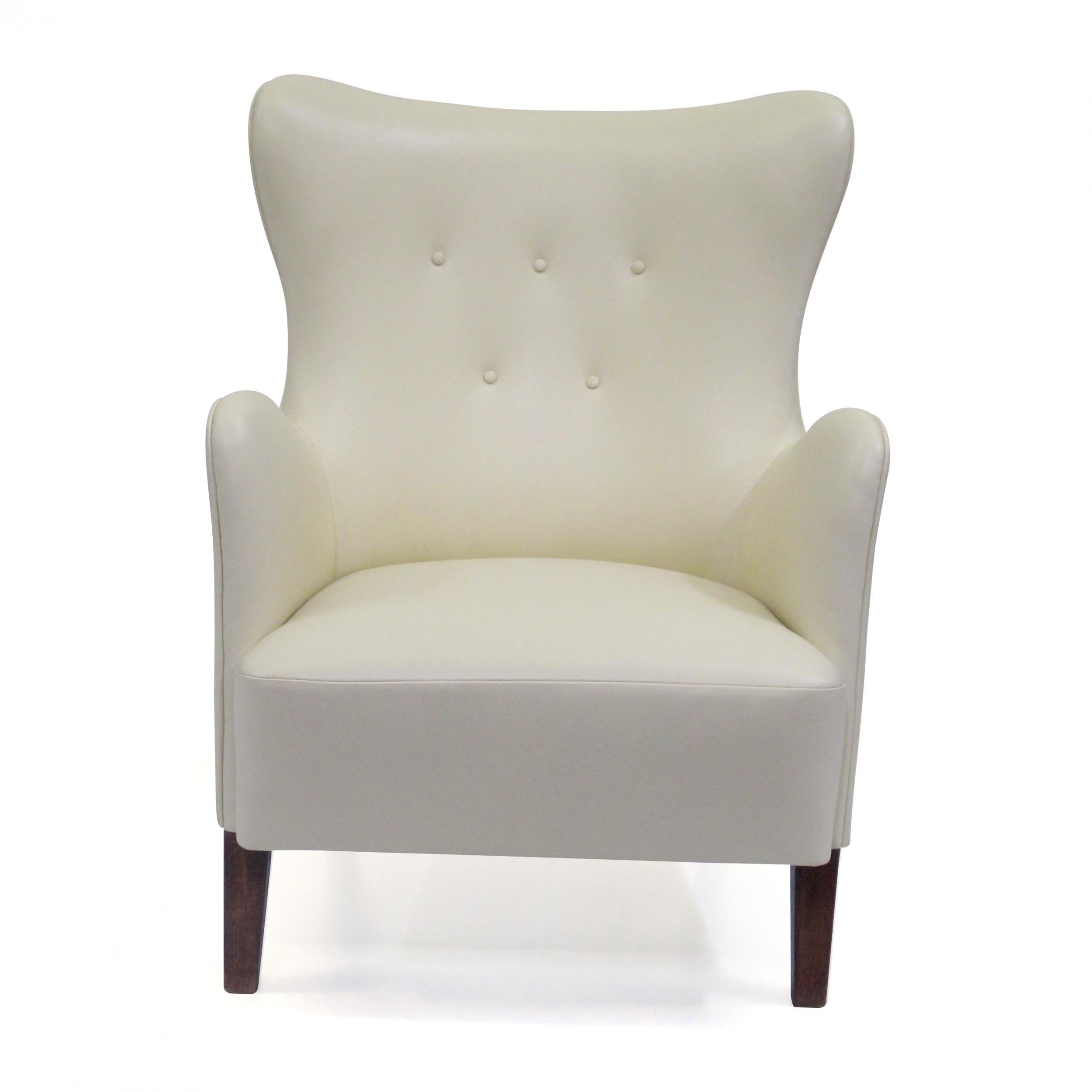Midcentury Scandinavian lounge chair crafted of a solid wood frame, hand-tied springs, and horsehair padding. The curved button-tufted backrest offers excellent back support. Newly upholstered in a soft cream color leather. Raised on walnut stained