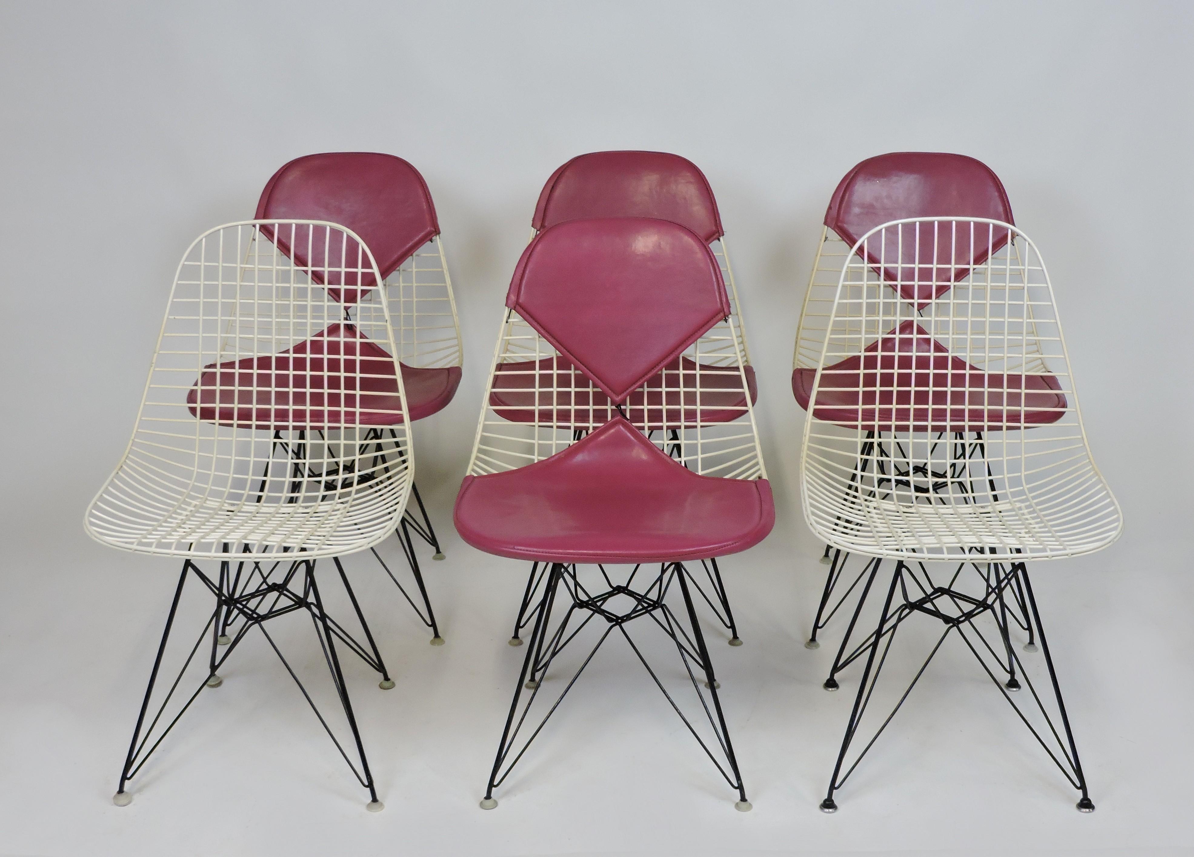 Very nice set of six early wire chairs designed by Charles and Ray Eames and manufactured by Herman Miller. These comfortable and light weight chairs have a white wire top and black Eiffel tower legs. Four of the chairs have magenta colored