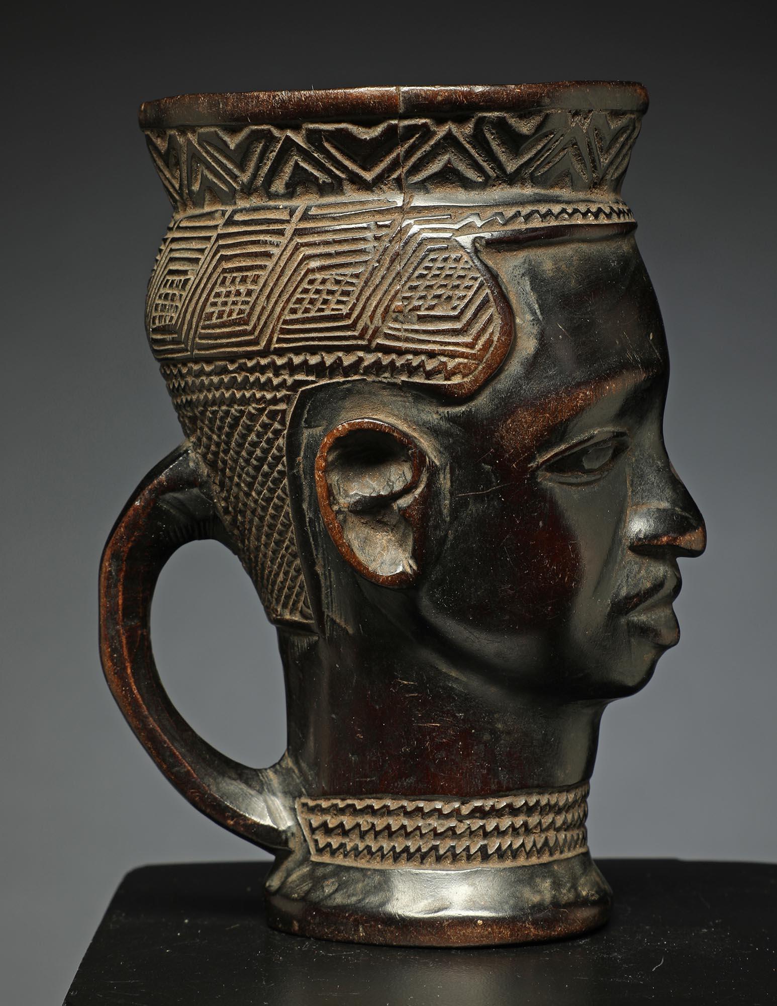 Small sweet early Kuba Cup with refinedf face, finely carved hair, with a handle, from the DRC, Africa
Finely incised hair in tight geometric form, small projecting ears.  Some damage and wear to lips, and small chips to rim.

It is in good