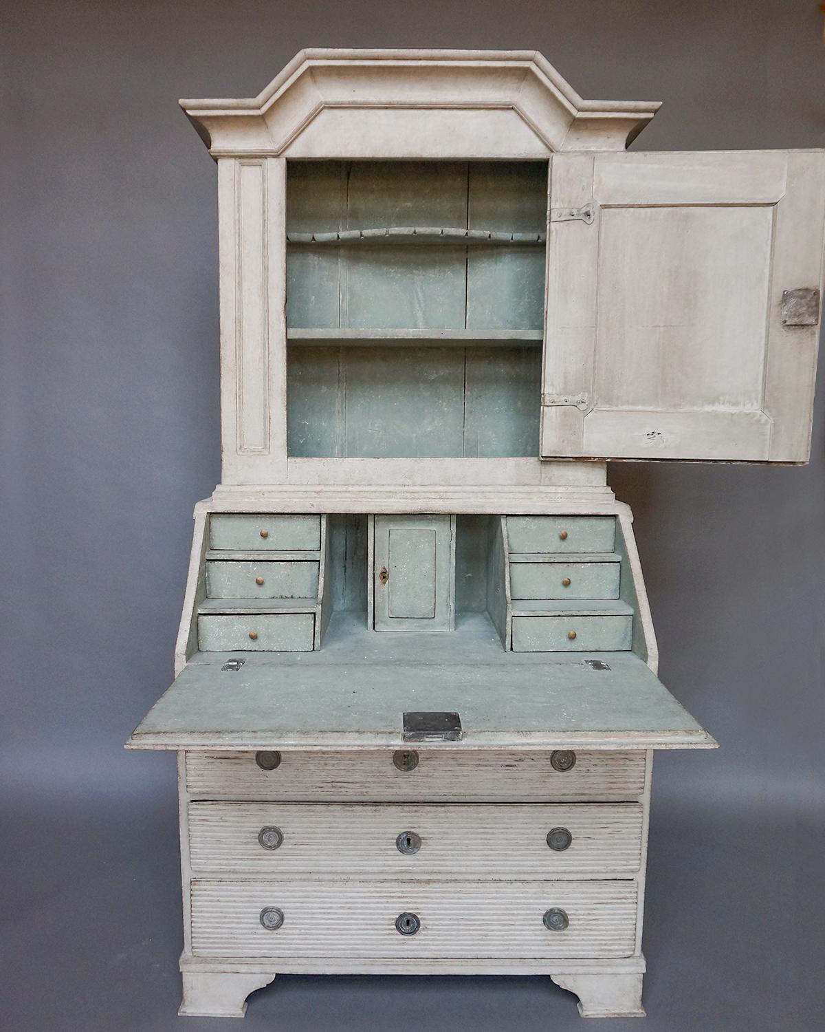 Slant-front secretary in two parts, Sweden circa 1790.  The upper section has an arched cornice and single paneled door, with two interior shelves, the top one shaped and notched for spoons.  The lower section has three full width drawers and a