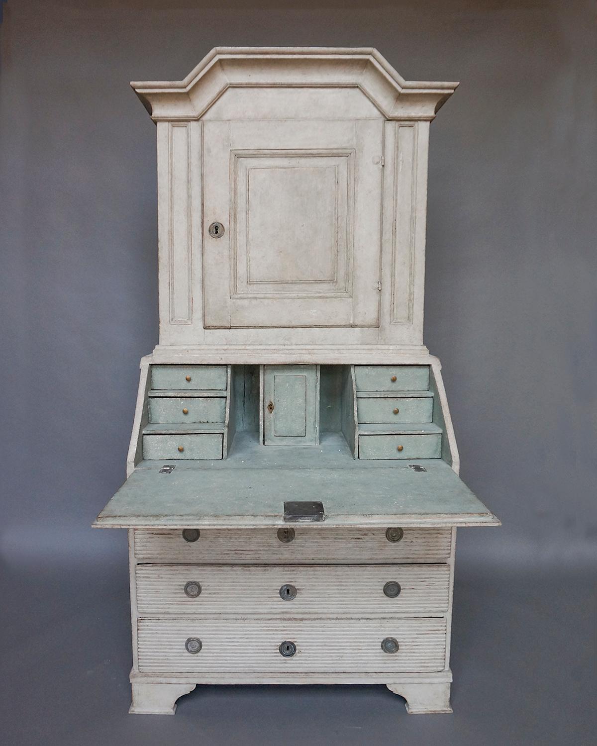 Slant-front secretary in two parts, Sweden, circa 1790. The upper section has an arched cornice and single paneled door, with two interior shelves, the top one shaped and notched for spoons. The lower section has three full width drawers and a