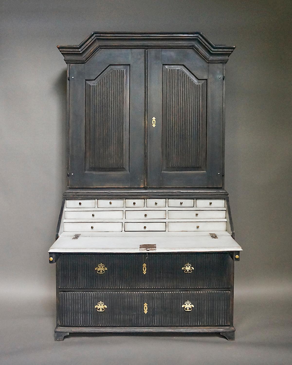 Early Swedish secretary in two parts, circa 1810. The upper section has a molded cornice with two raised and reeded panel doors. Inside are three fixed shelves, the top one shaped and notched for spoons. The lower section has a triple bank of small