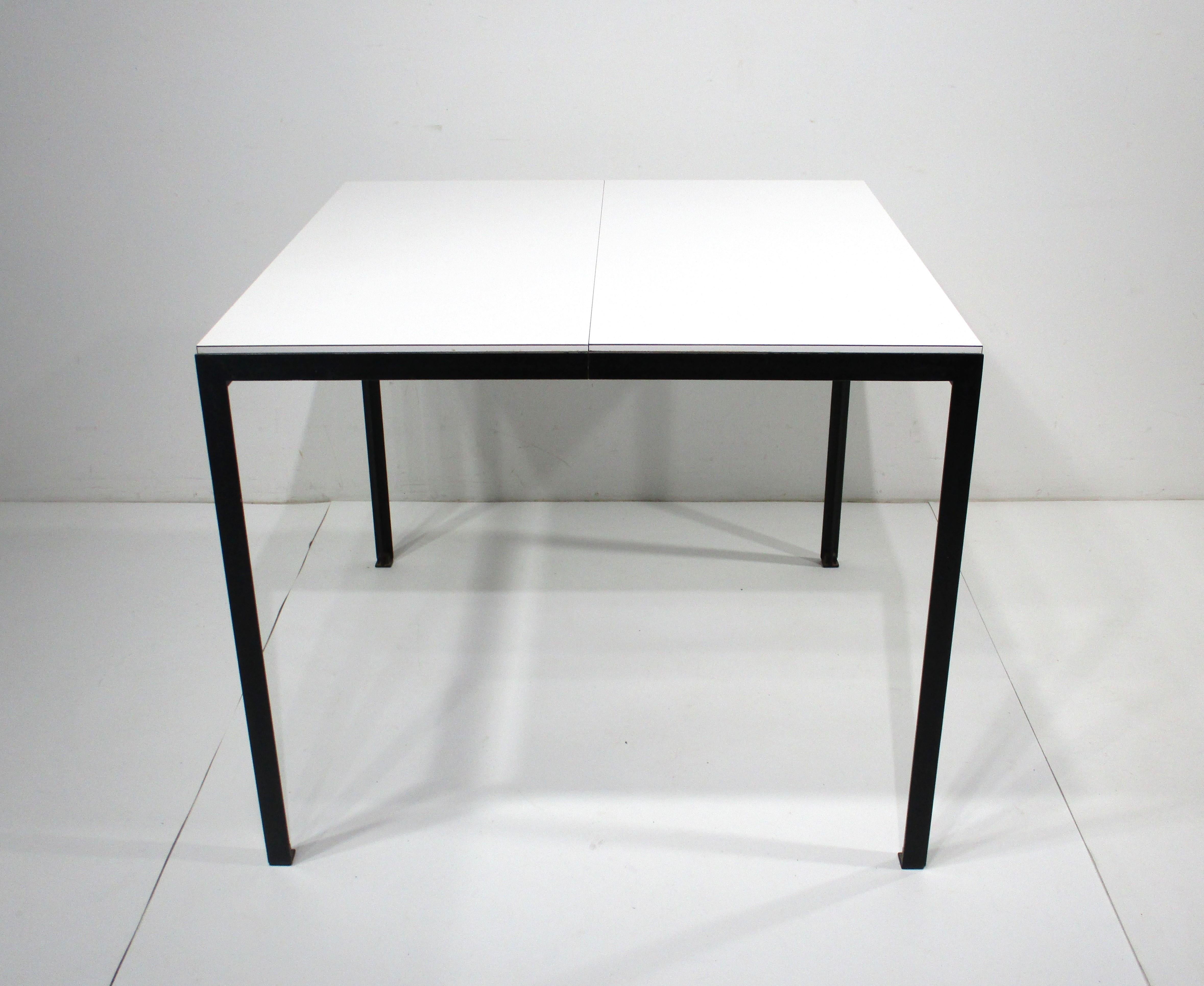 A well crafted smaller extension dining table with white Laminate top and satin black angled steel base with foot pads . This brilliant design has a folding pop up table leave that is connected to the underside of the table , just spread the table